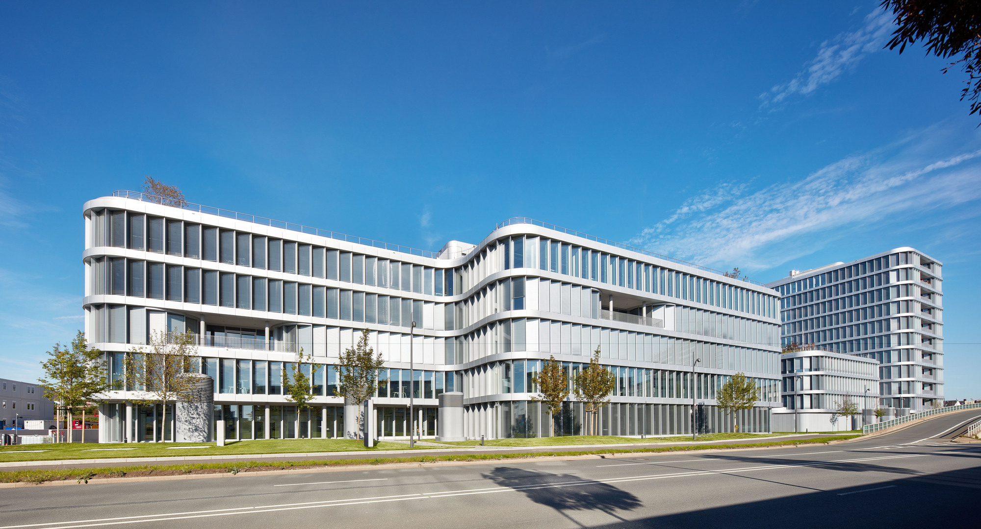 Curving office block with banded white facade and rows of glazing beside an empty road under a clear blue sky