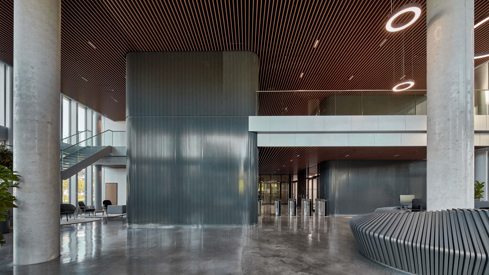 Lobby with concrete columns, a corrugated metal core, a slatted timber ceiling and a ribbed reception desk with ring lights