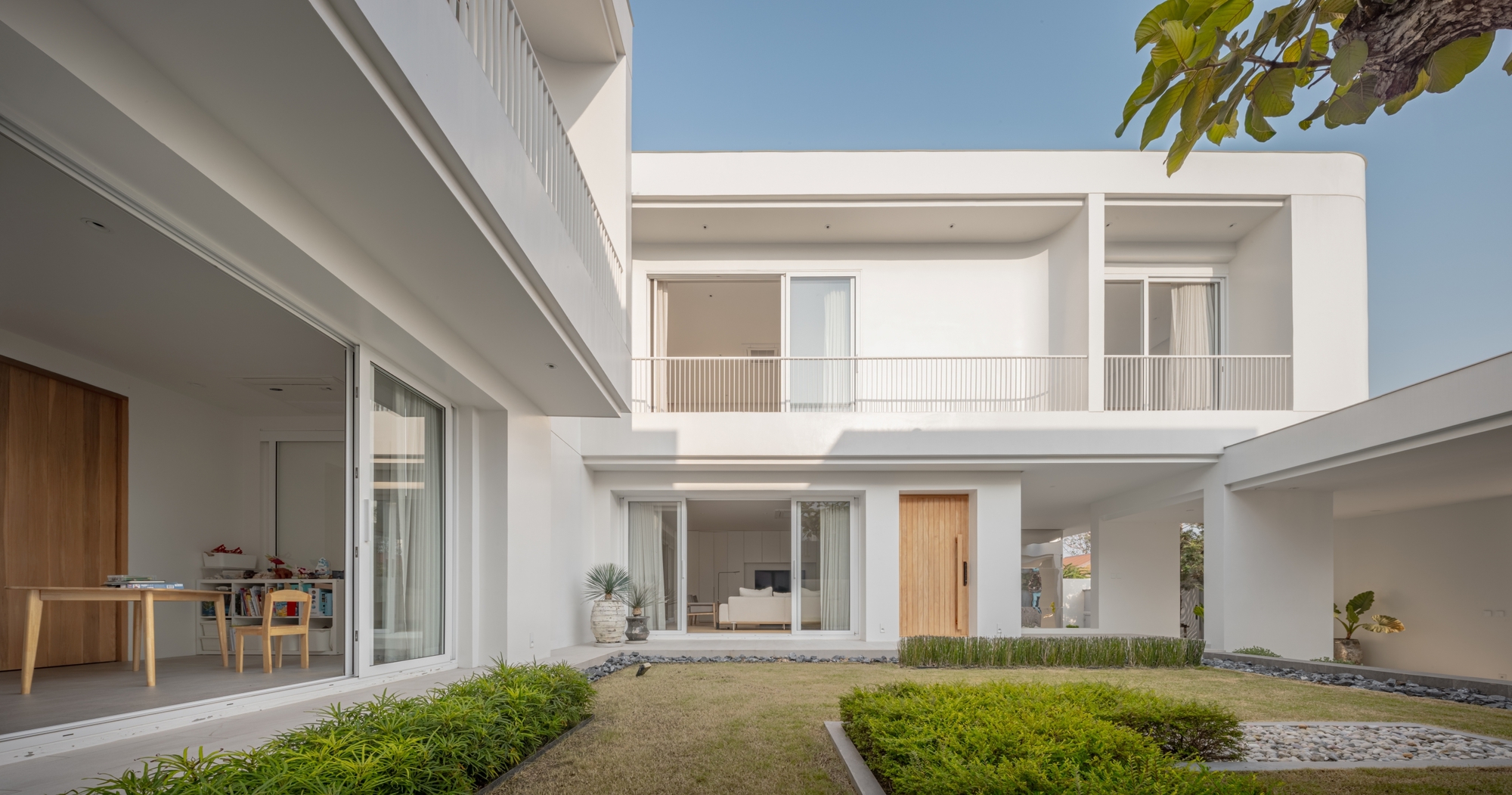 Courtyard elevation with sliding glass doors, a timber front door and clipped hedges on a lawn in afternoon sun