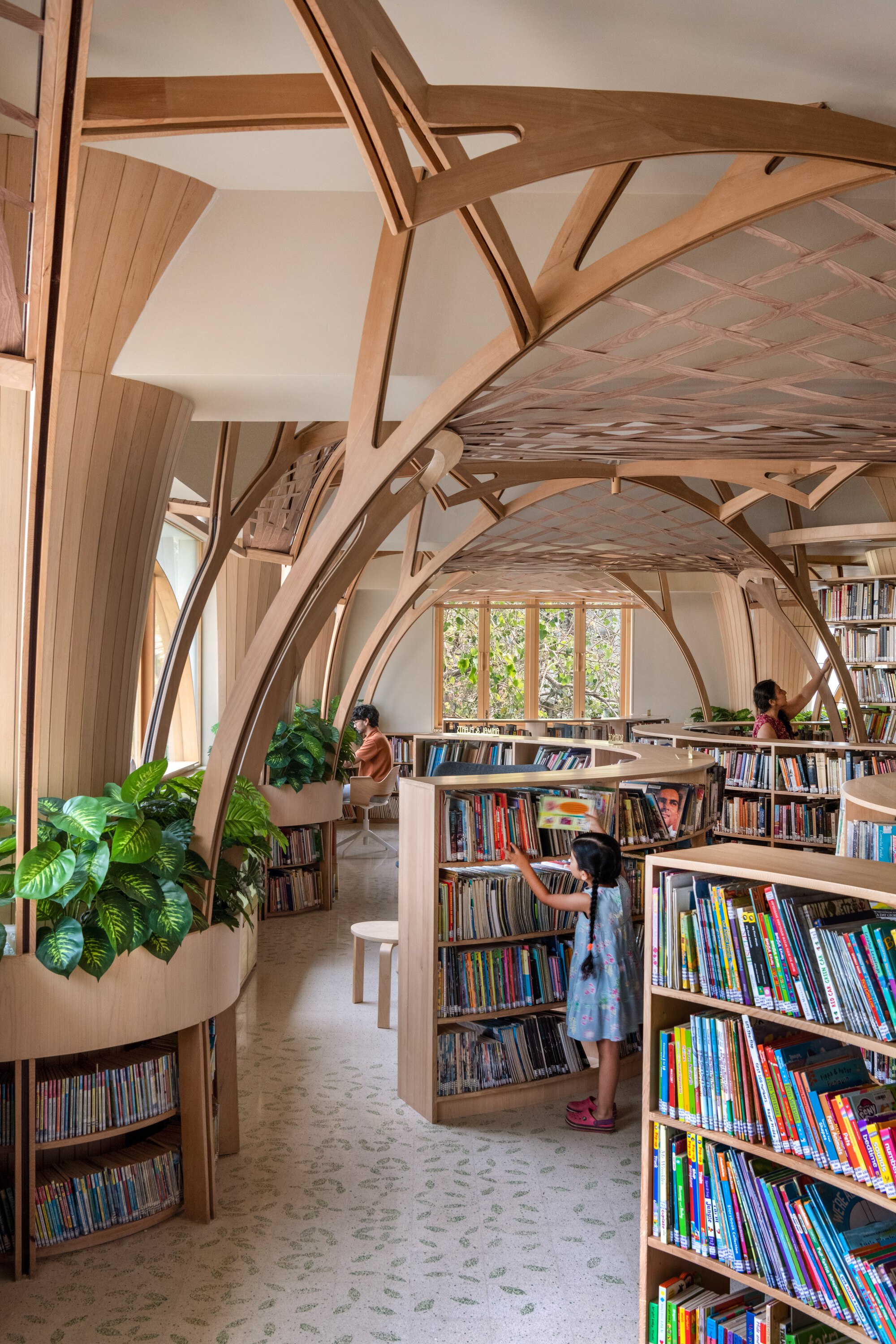 Children's library aisle with curved timber ribs, planter-topped shelving and a girl reaching for a book in soft daylight