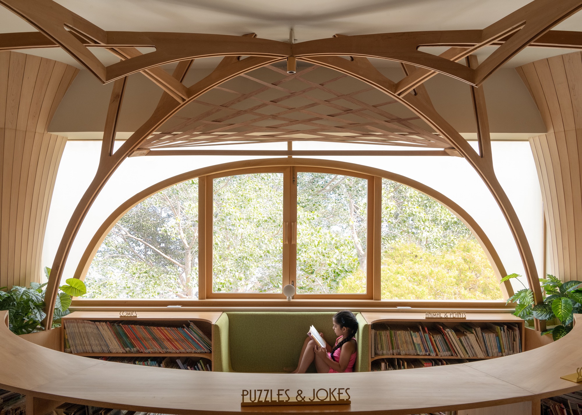Girl reading on a green window seat inside a half-round arched window, framed by timber ribs and a curved counter