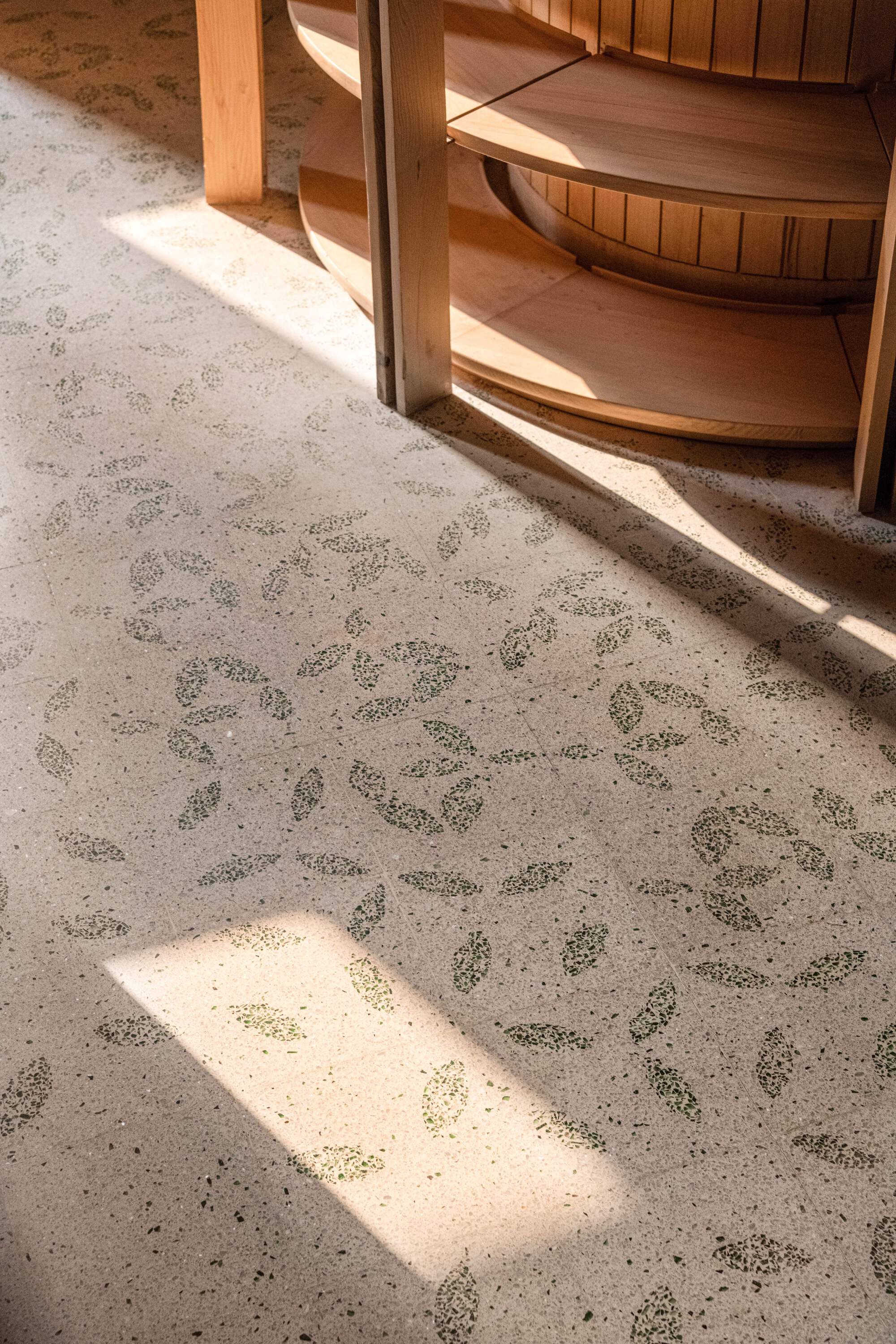 Terrazzo floor with a green leaf pattern, crossed by bands of sunlight near the base of round timber shelving