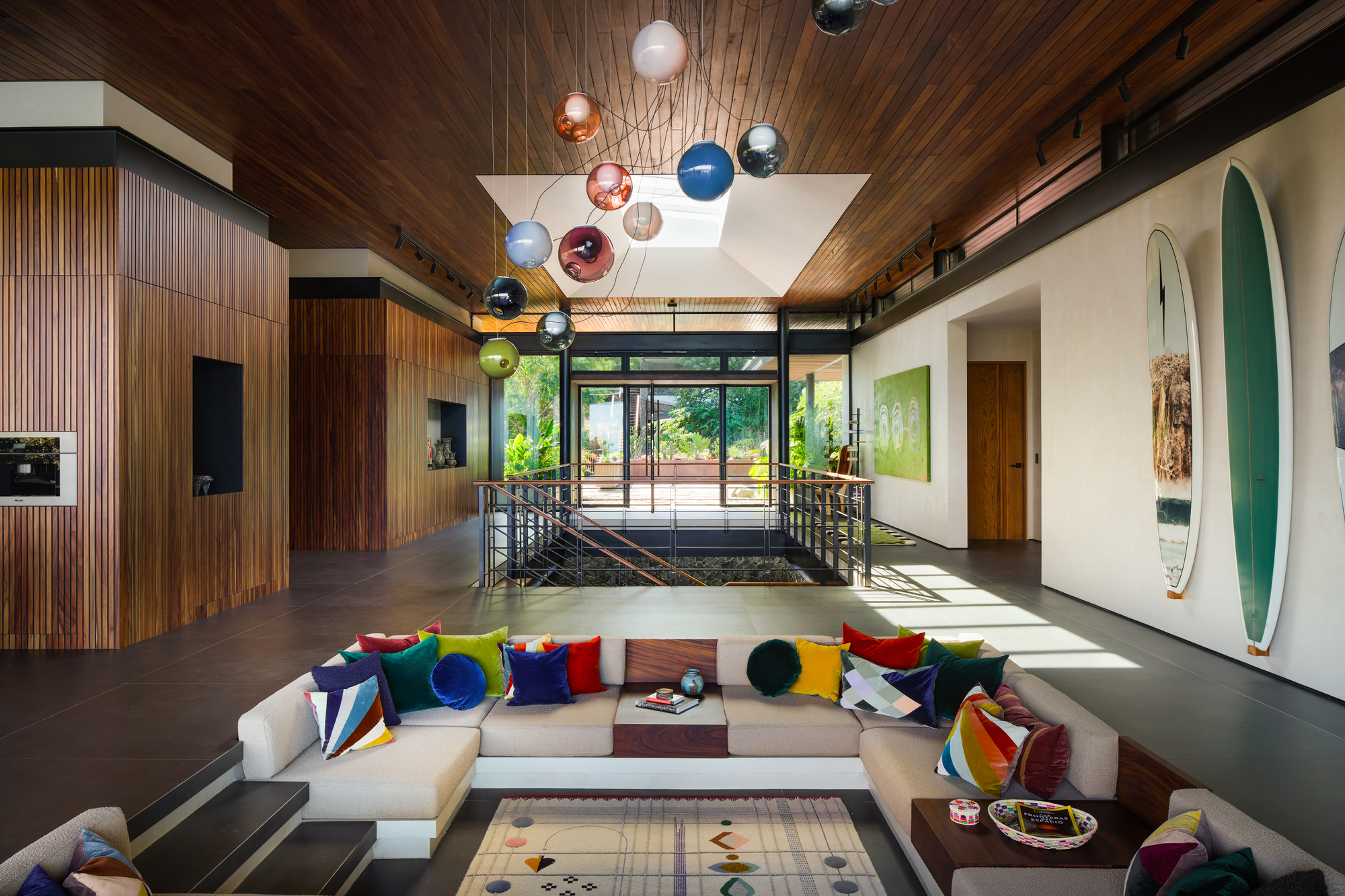 Double-height living room with a sunken sofa pit, glass globe pendants and surfboards on the wall under a skylight