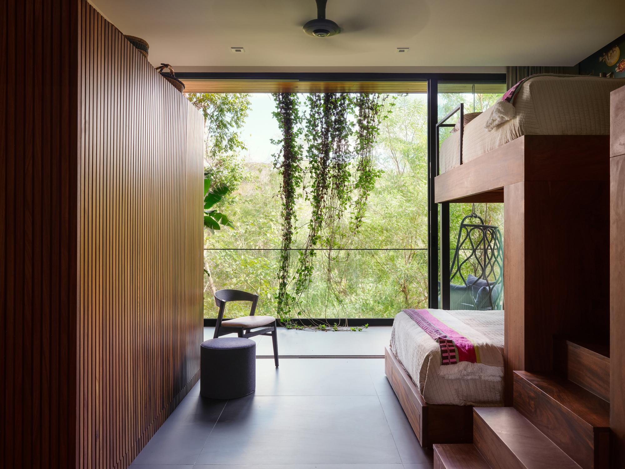 Bedroom with slatted wood wall and bunk beds facing a glass wall hung with trailing vines