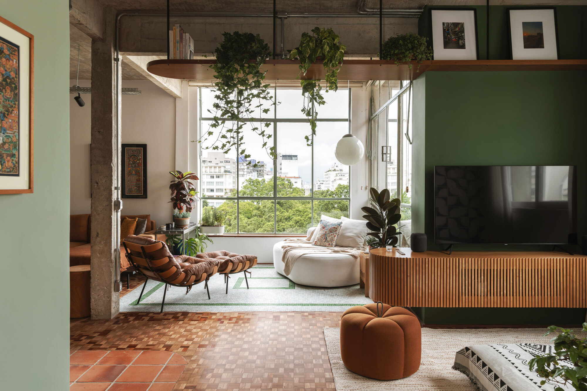 Sitting corner framed by a hanging timber shelf of trailing vines, with a green wall and fluted media cabinet at right