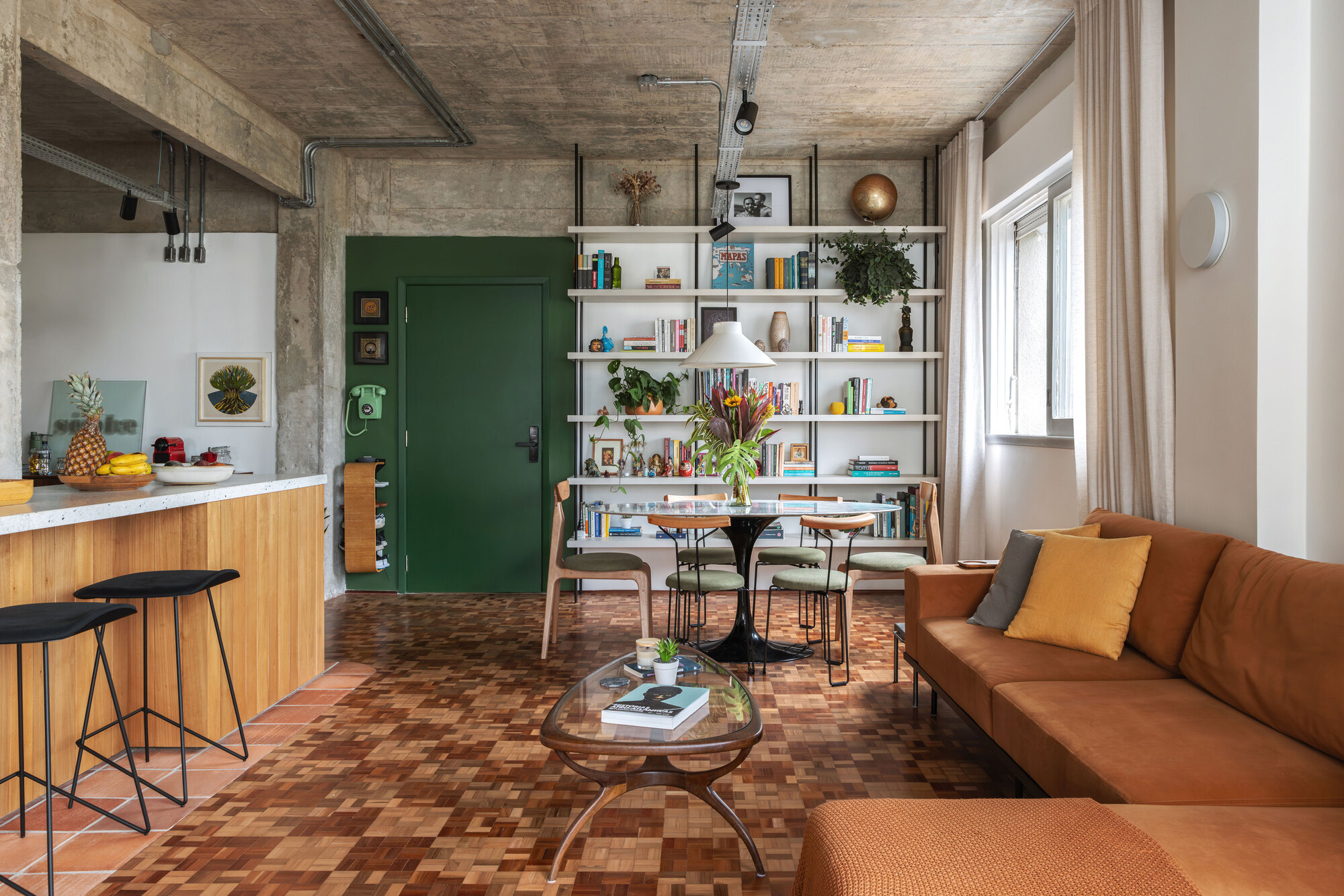 Dining area with a white bookshelf wall, green door and parquet floor, with a tan sofa and cushions in the foreground