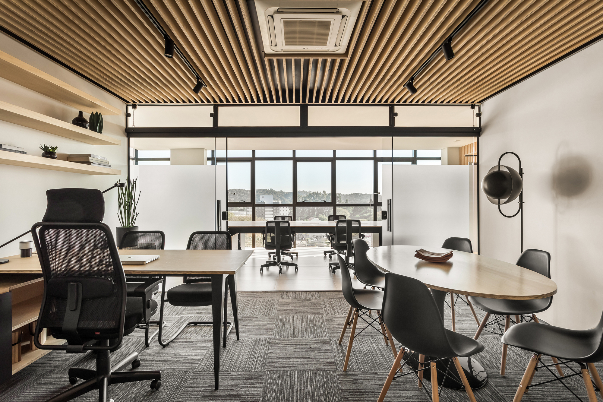 Meeting area with an oval table and black shell chairs beneath a timber slat ceiling, with hills visible through the glazing beyond