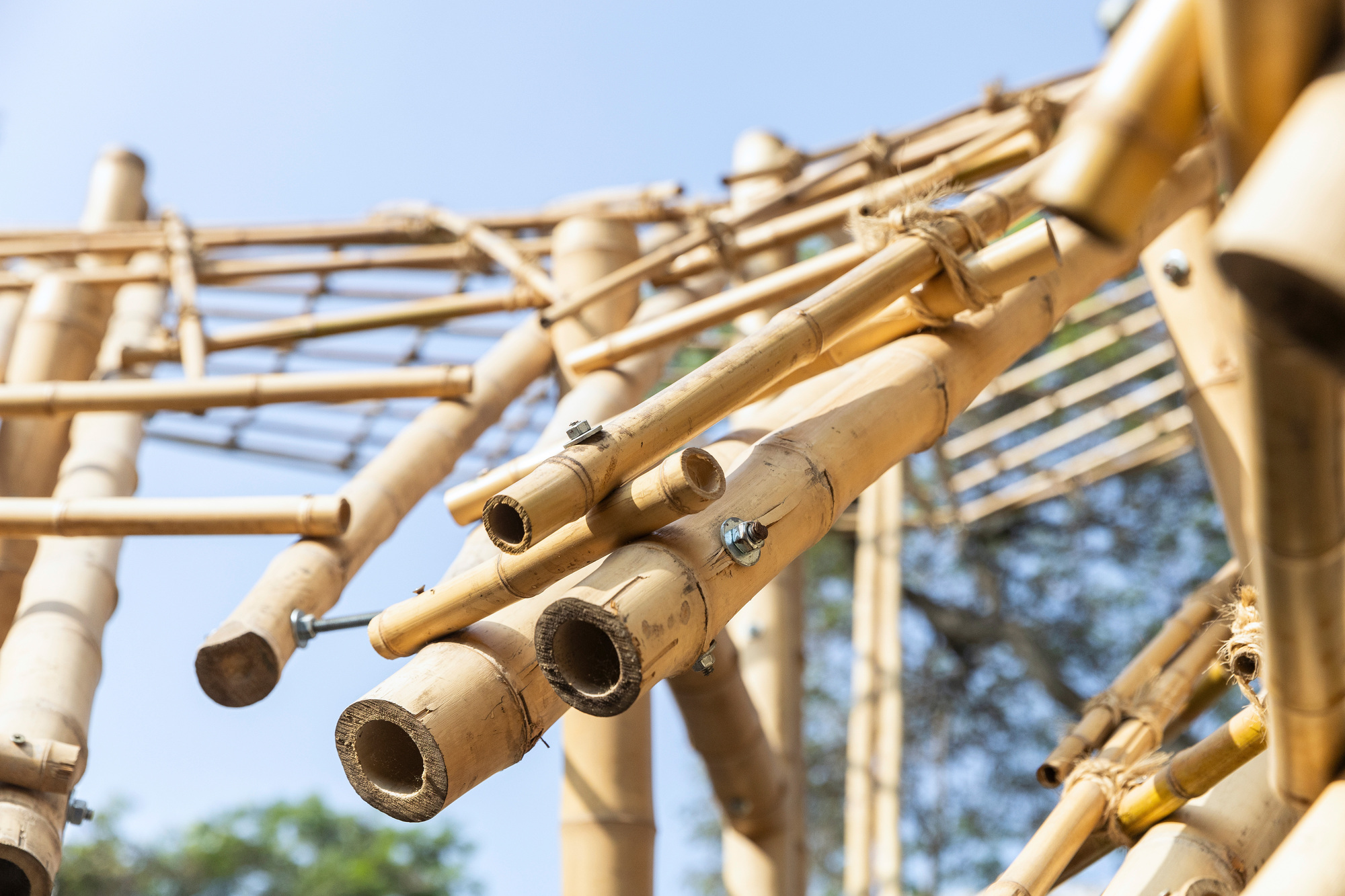 Close-up of bamboo poles joined with bolts and rope lashing, their open ends facing a clear blue sky