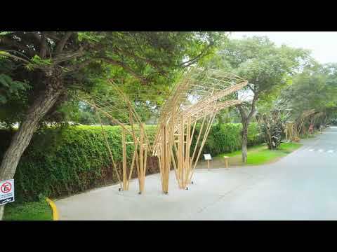 Bamboo petal-shaped canopies standing along a paved path beside a clipped hedge and street trees on an overcast day