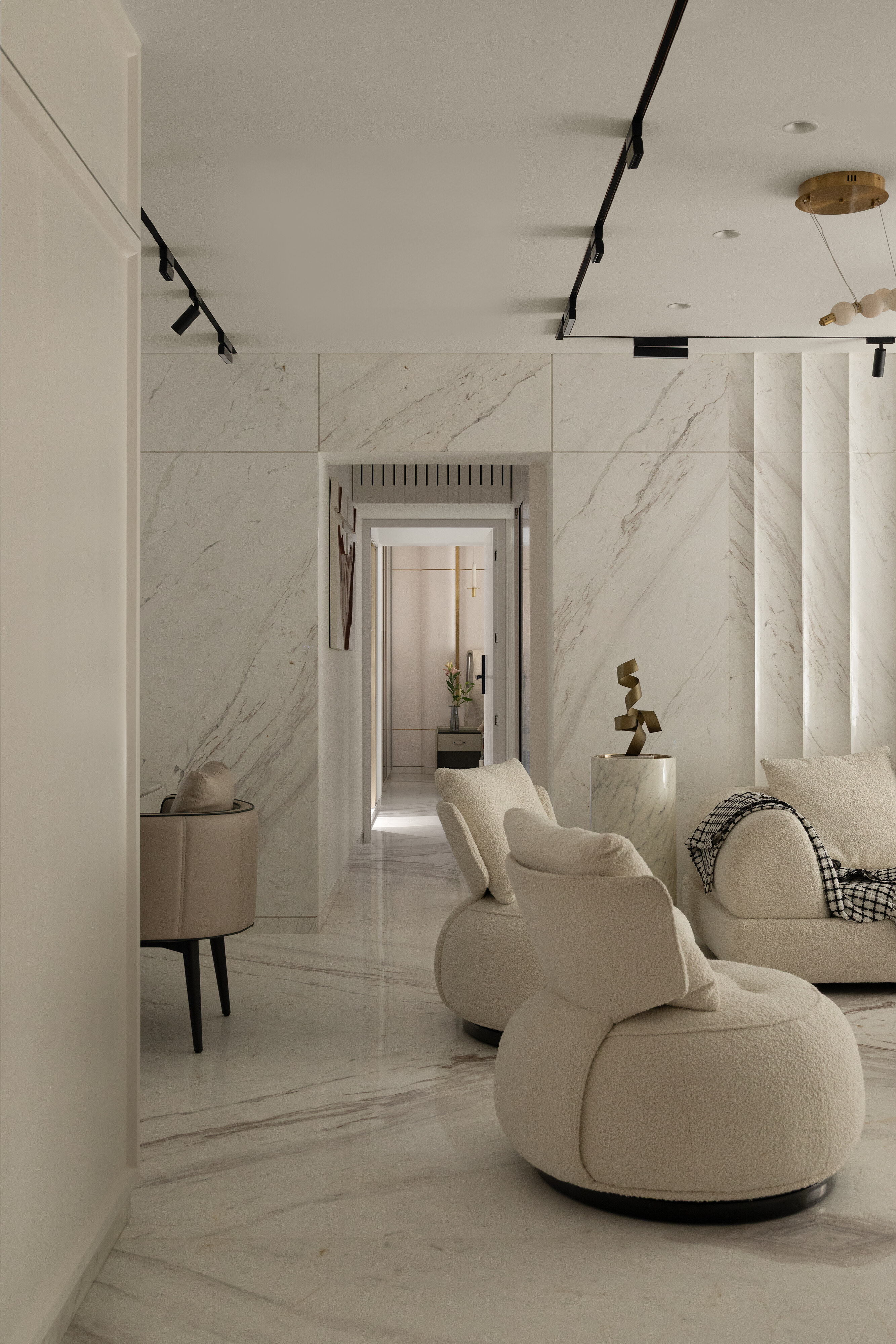 A marble-clad transitional corridor connecting the living room to the private quarters, with bouclé swivel chairs and a brass sculpture on a marble pedestal.