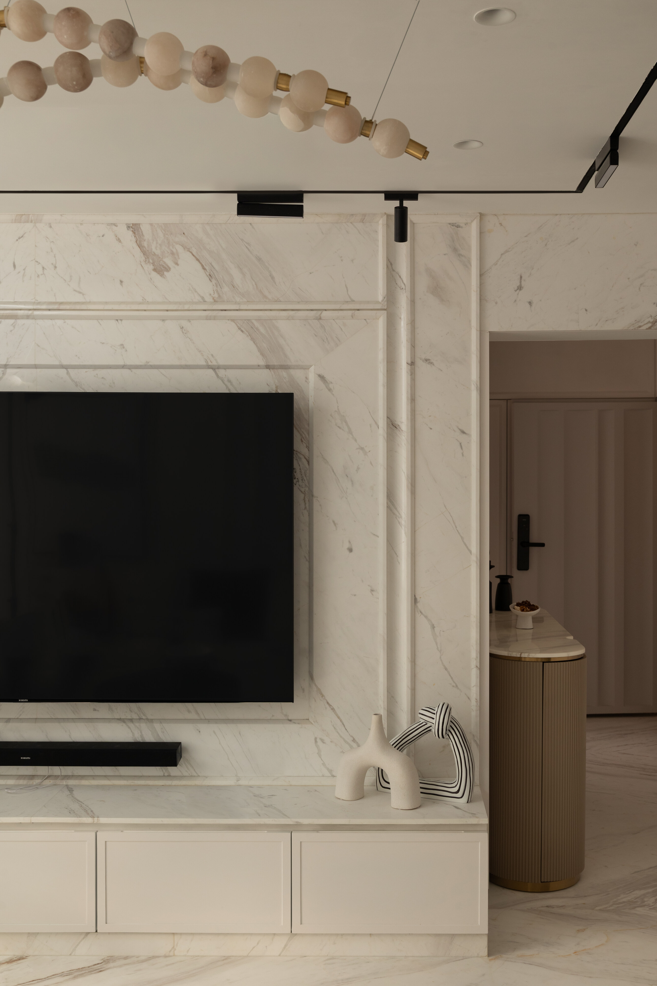 The media wall, with a carved marble frame and a curved fluted side cabinet in brass.