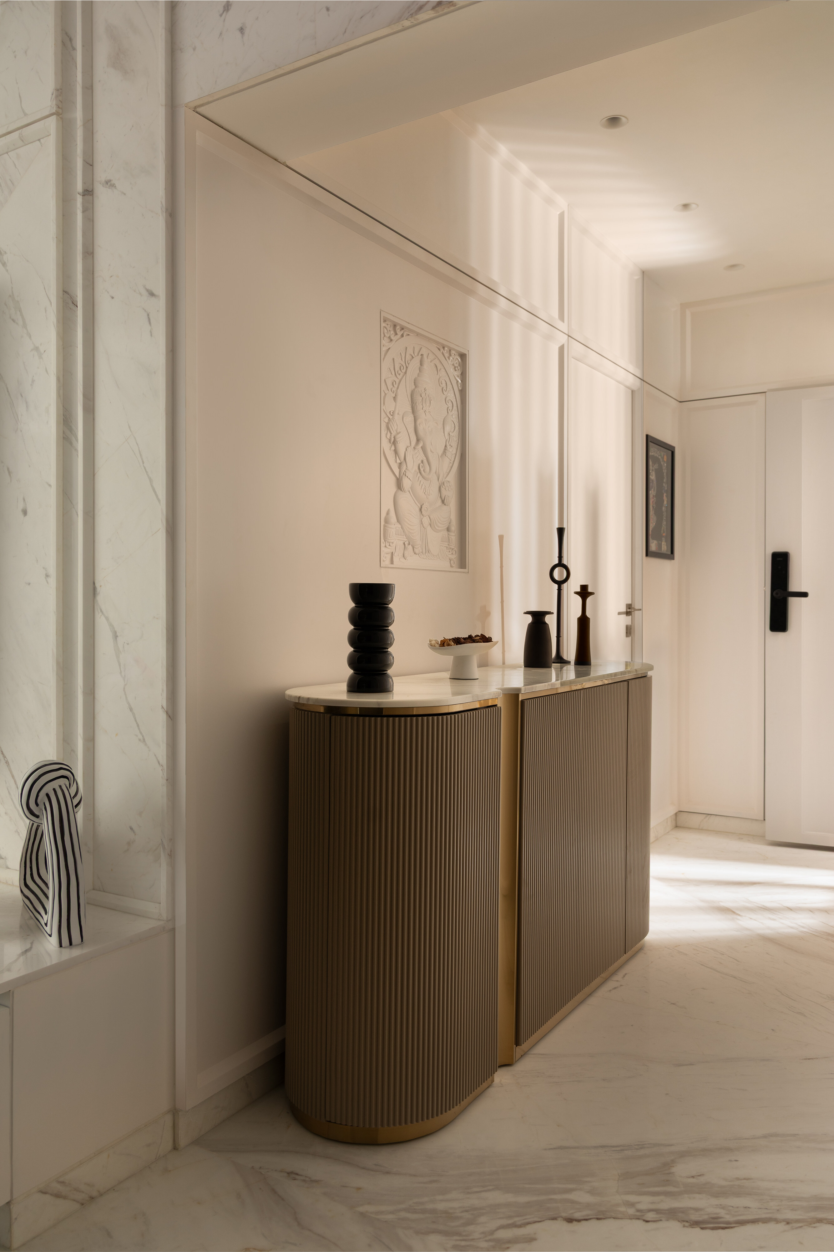 The foyer console: a fluted brass-banded cabinet with a carved Ganesh relief above.