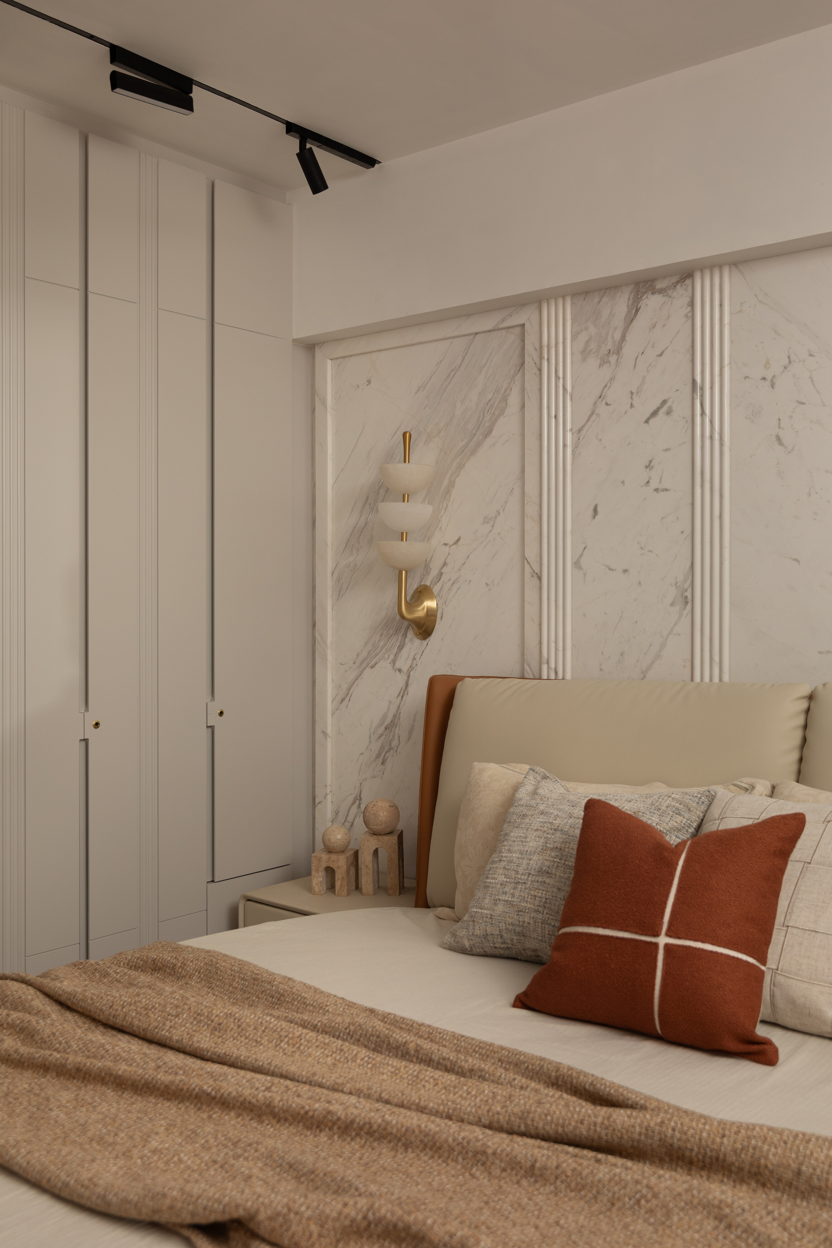 A bedroom with a book-matched marble feature wall and a brass-and-alabaster wall sconce.