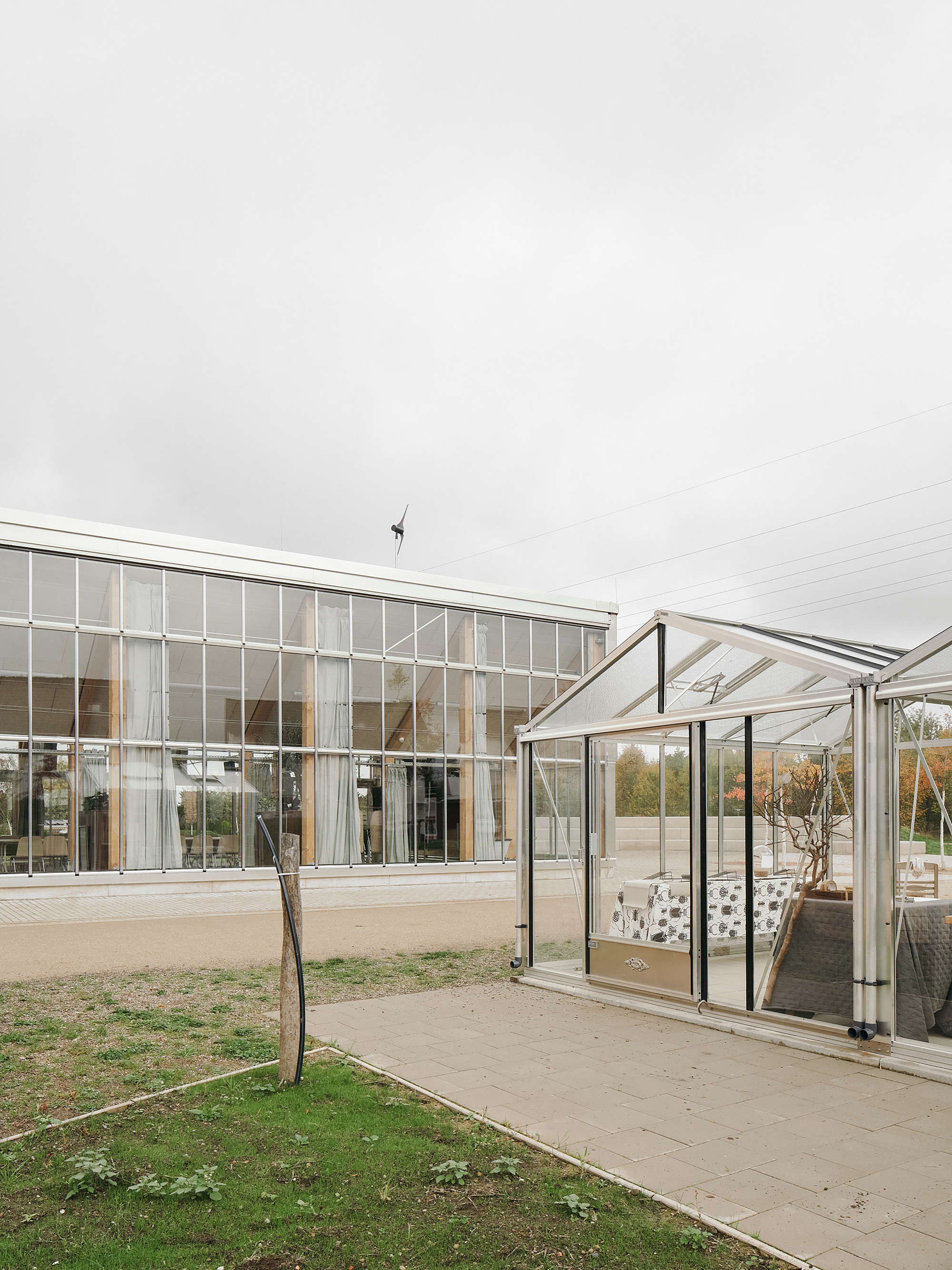 Glazed long facade with an adjacent small greenhouse and a wind turbine on the ridge