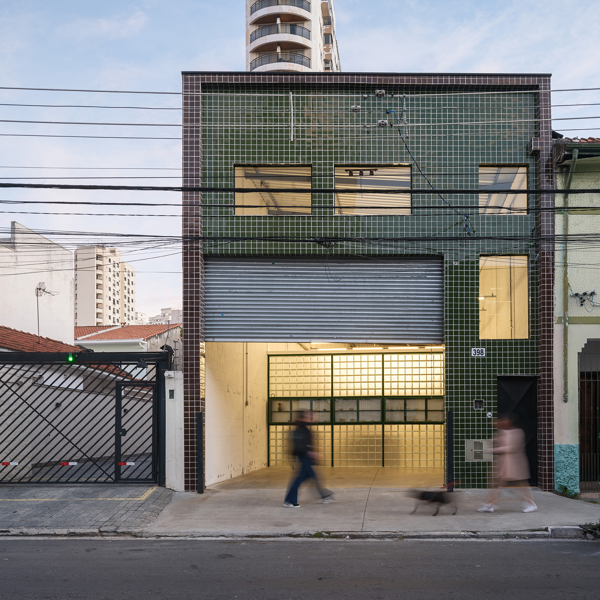 Street facade with glass block tiles and green metal frames as pedestrians pass at dusk