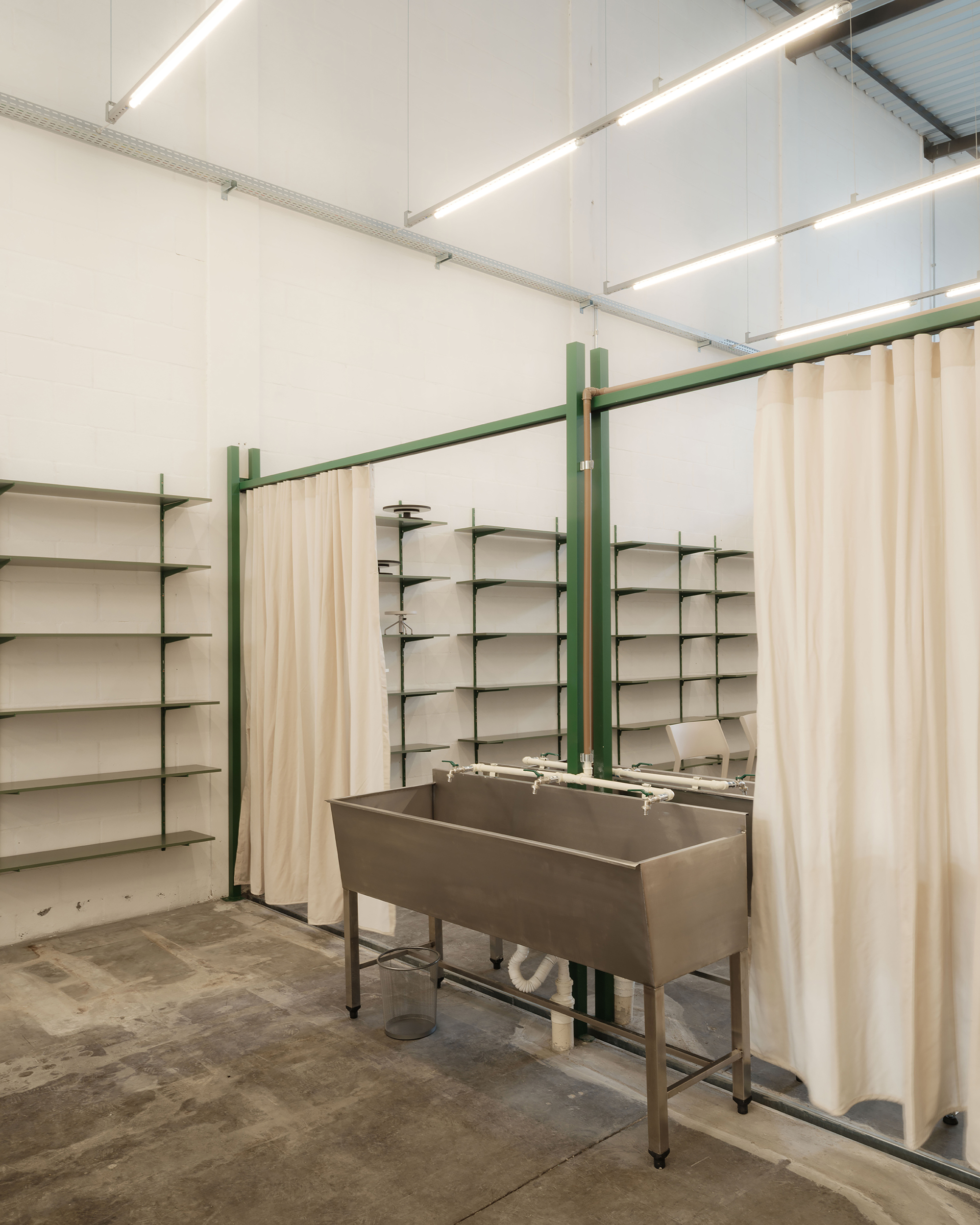 Stainless steel wash basin on green frame with open shelving and cream curtains behind