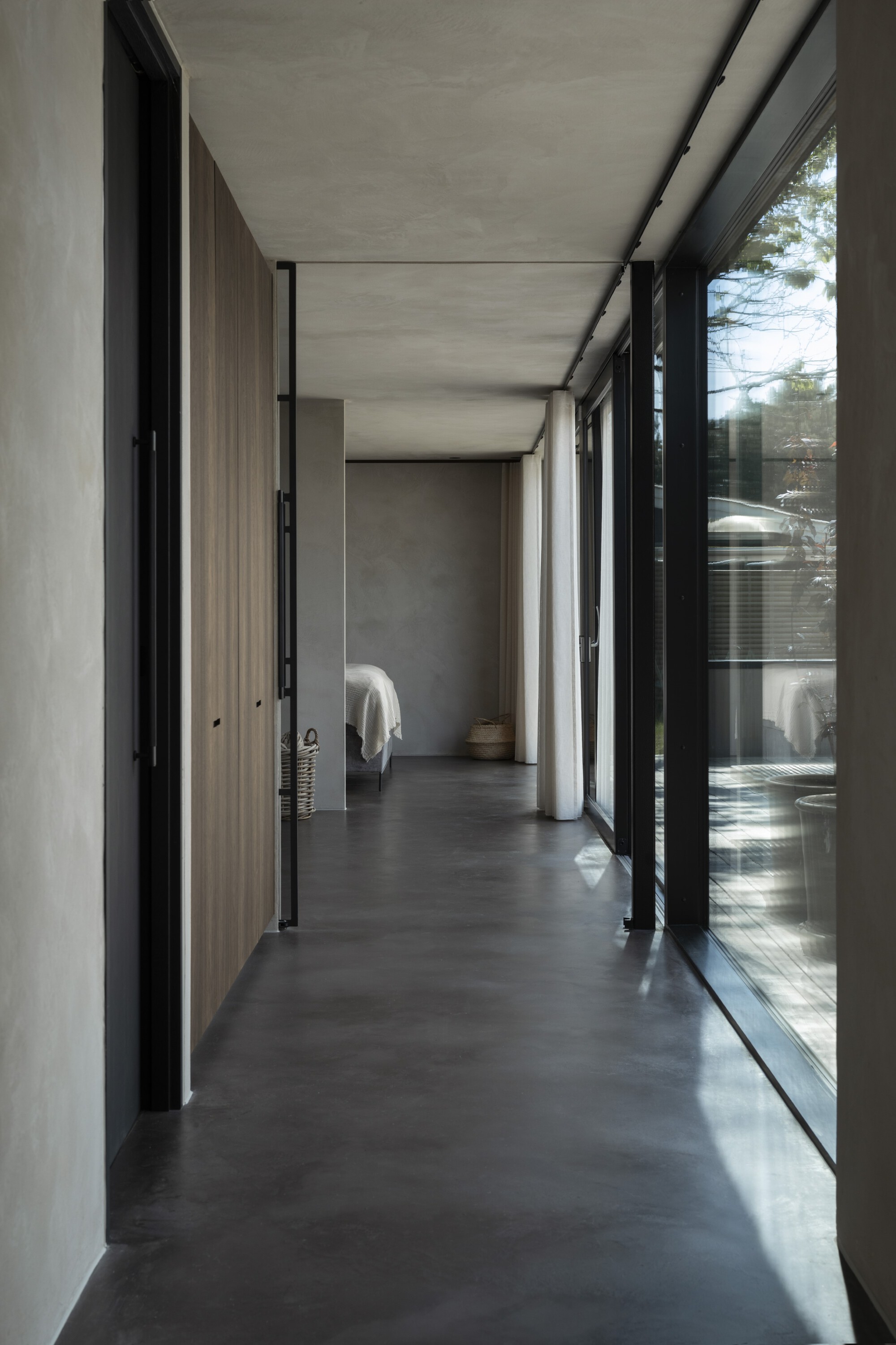 Corridor with polished concrete floor flanked by floor-to-ceiling glazing and timber-clad walls