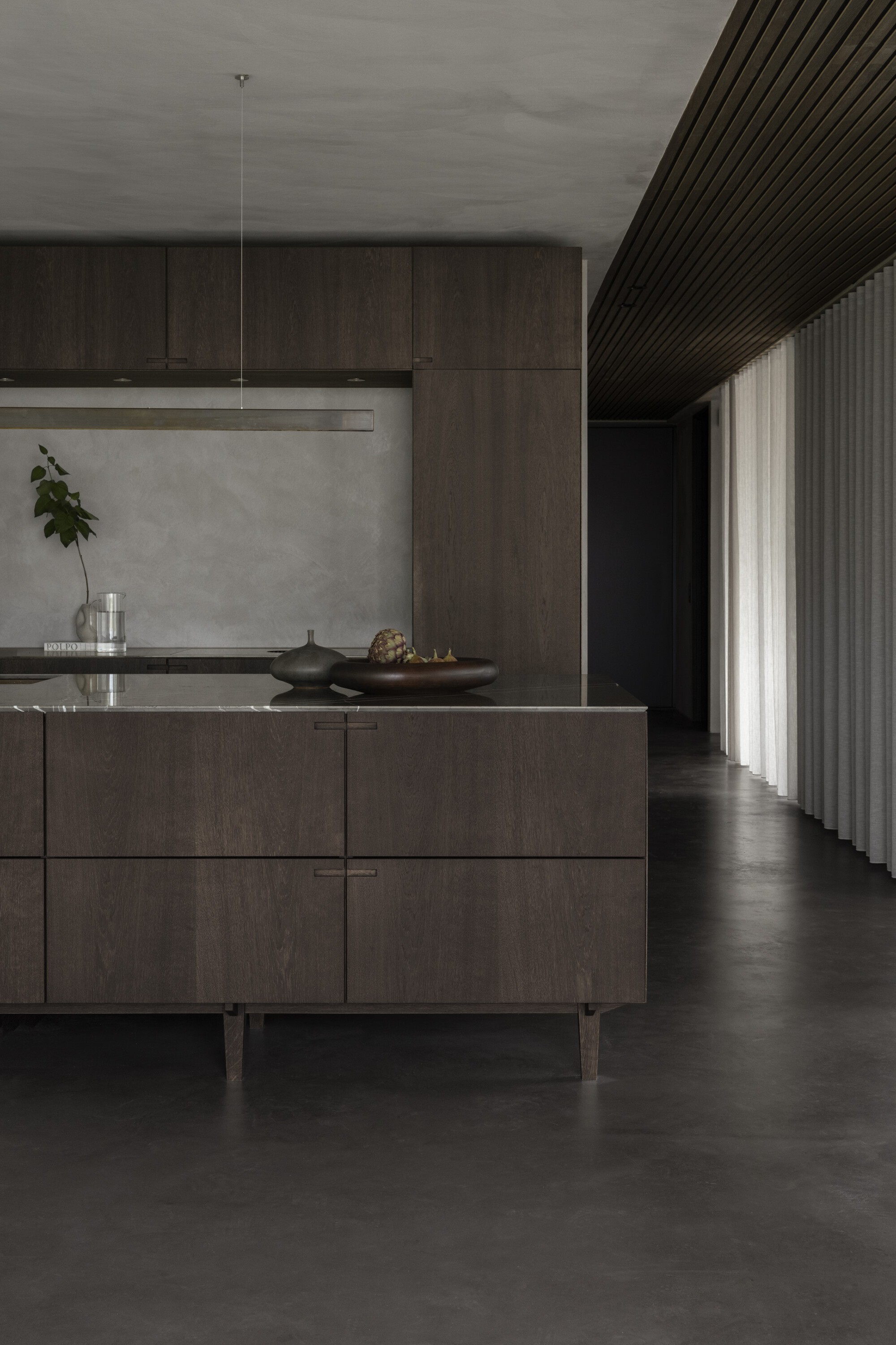 Kitchen island with timber cabinetry beneath a slatted timber ceiling and floor-length curtain