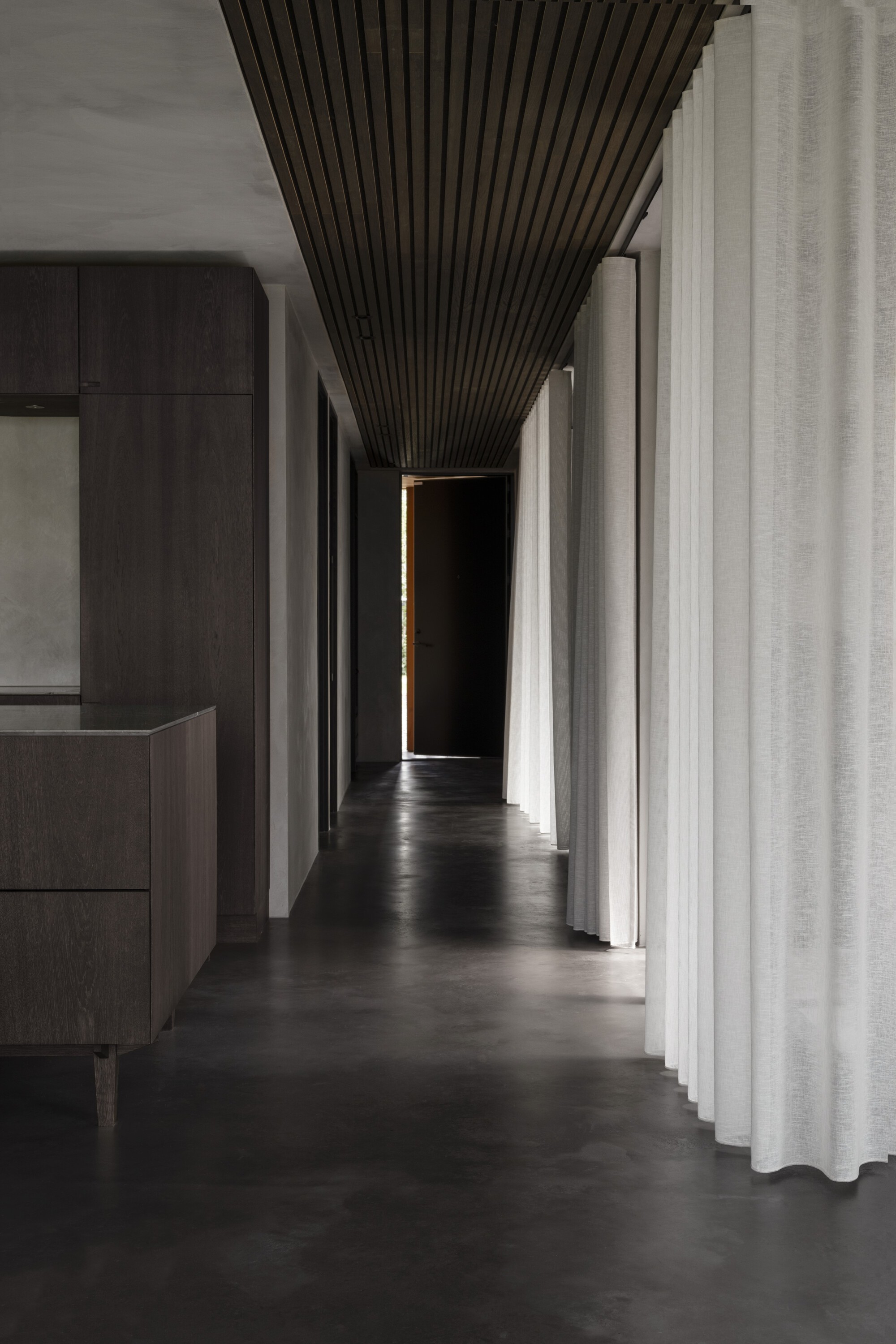 Corridor with dark slatted ceiling tapering toward a doorway illuminated by a narrow strip of light