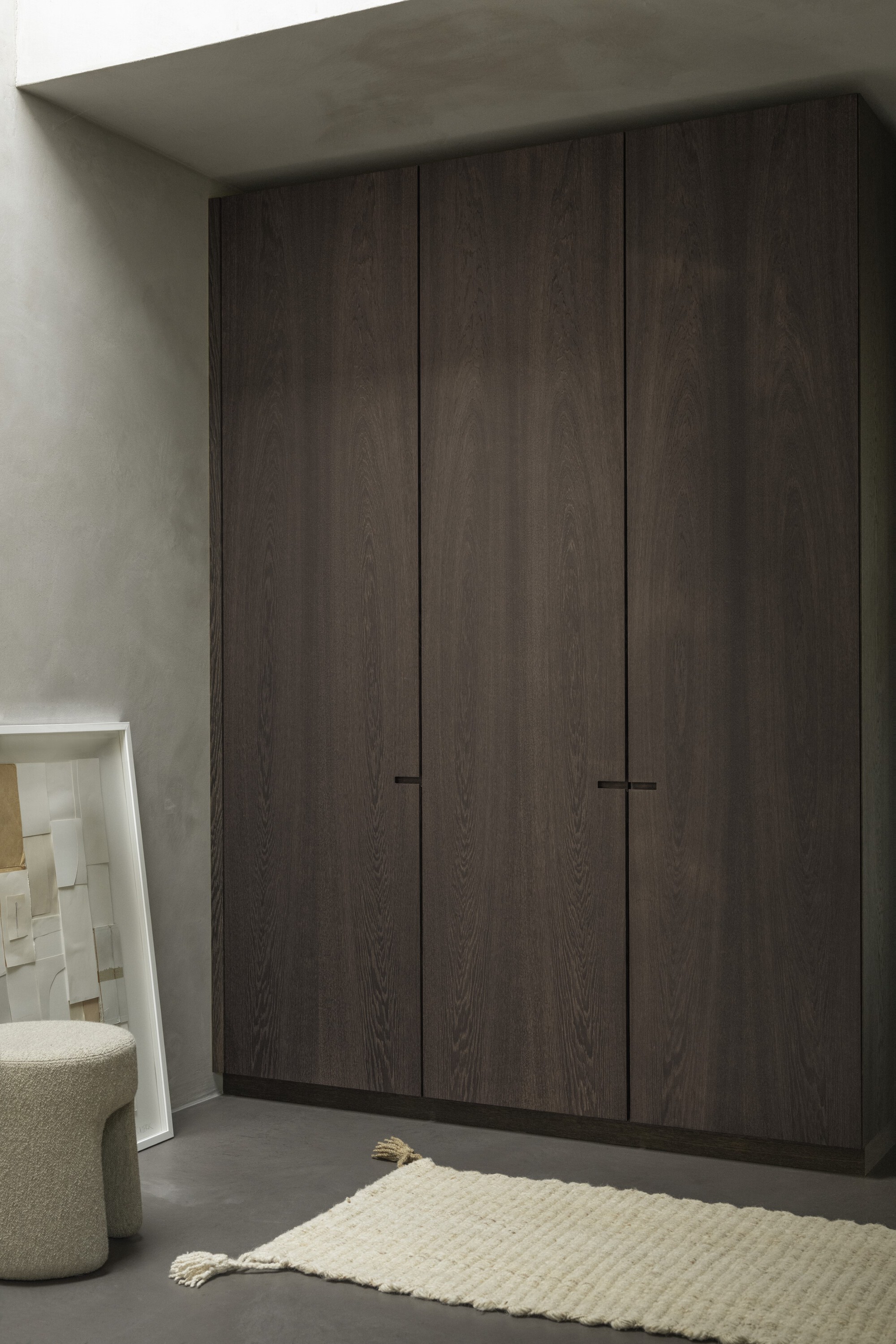 Floor-to-ceiling dark oak wardrobe with minimal black handle detail against pale plaster walls