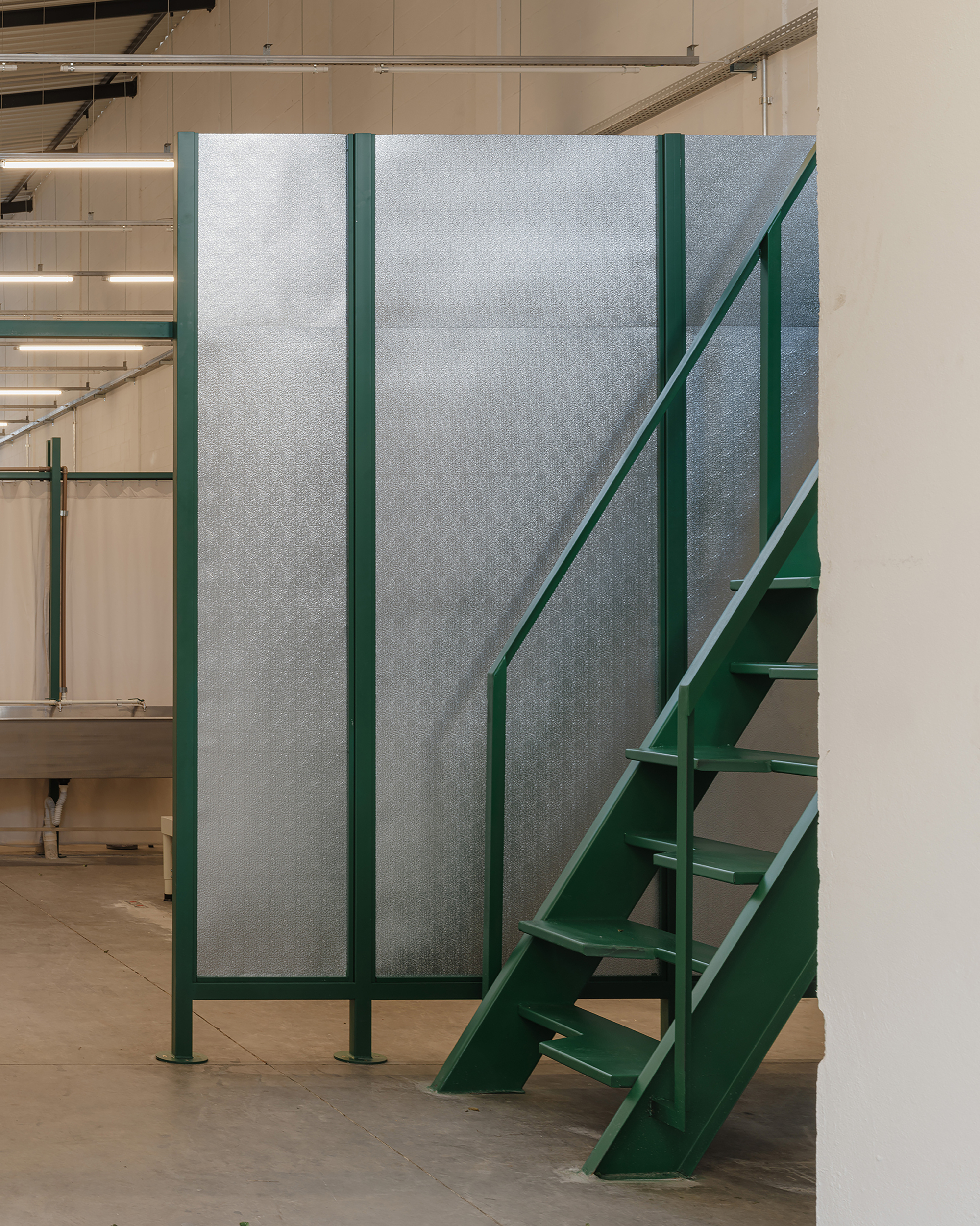 Green steel staircase ascending beside a partition of translucent panels framed in matching green steel