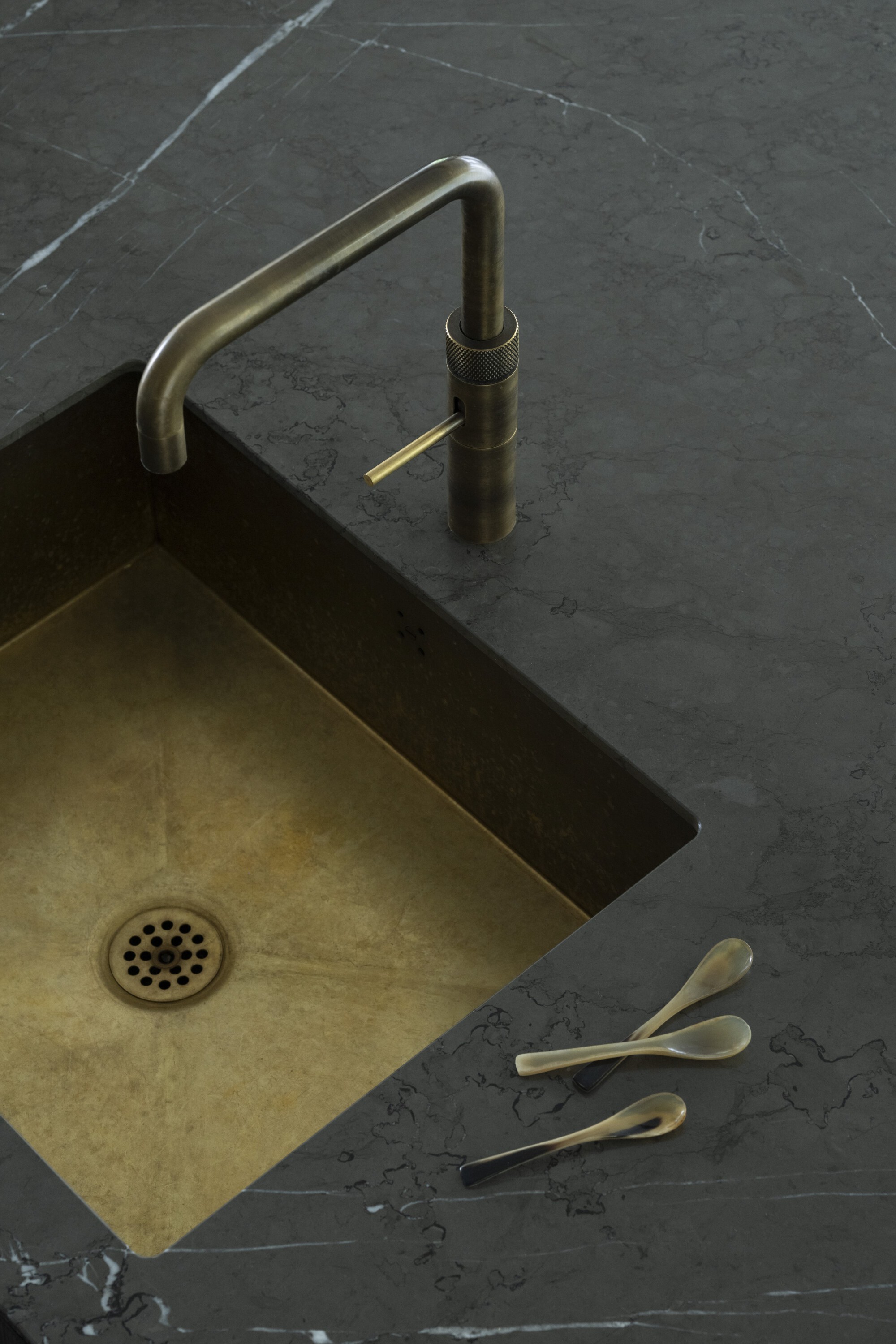 Brass sink faucet and undermount basin set into dark marble countertop with veining