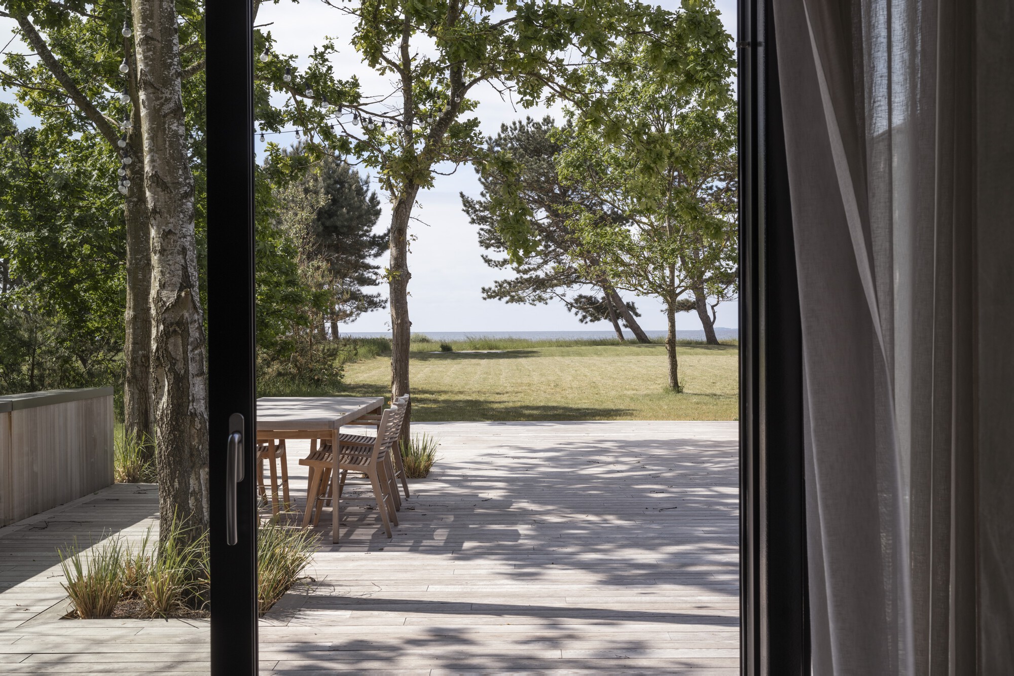 Timber deck framed by black sliding doors opening to lawn and coastal trees
