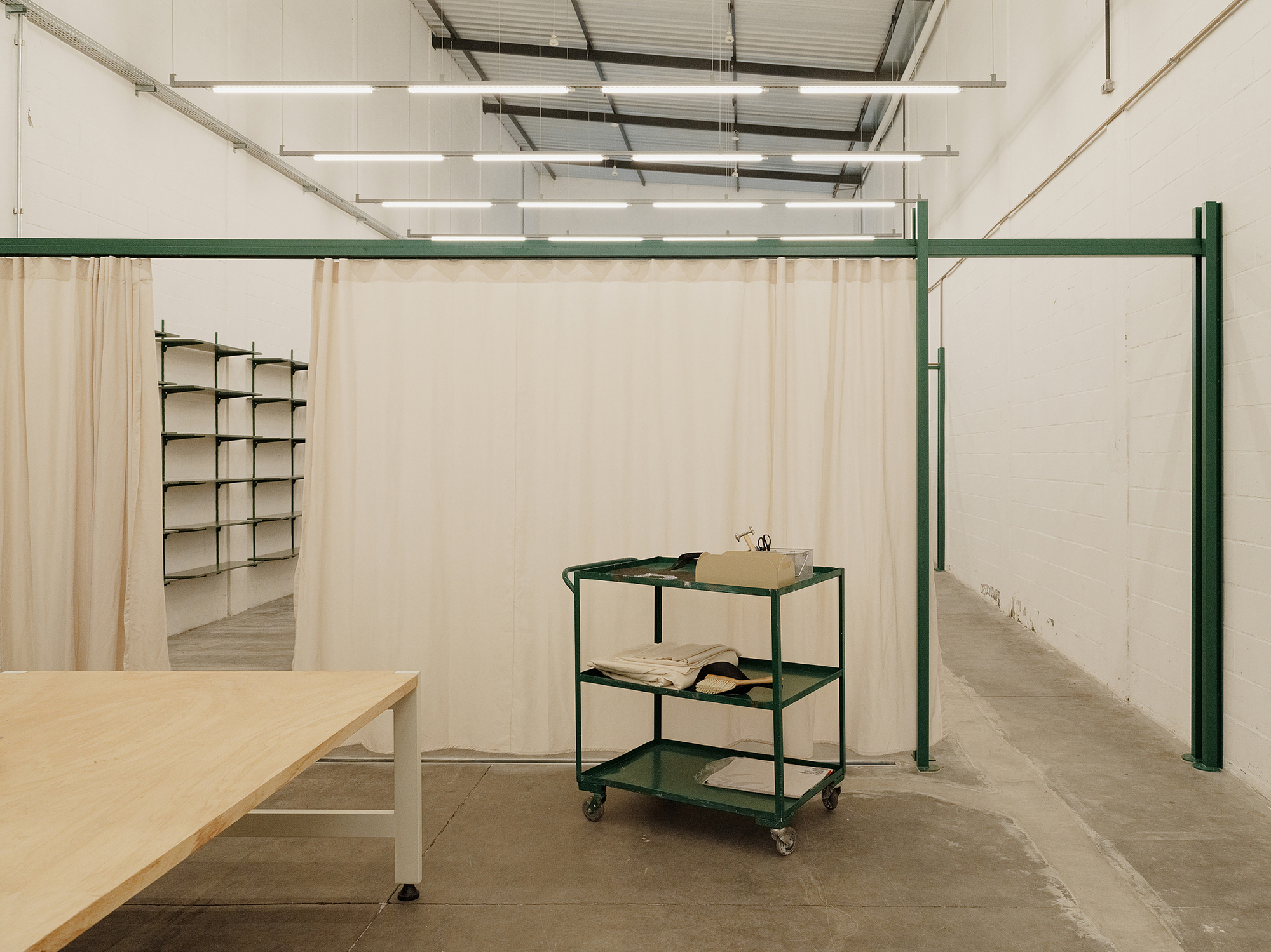 Green steel framing system with fabric panels dividing the workspace and a three-tier rolling cart