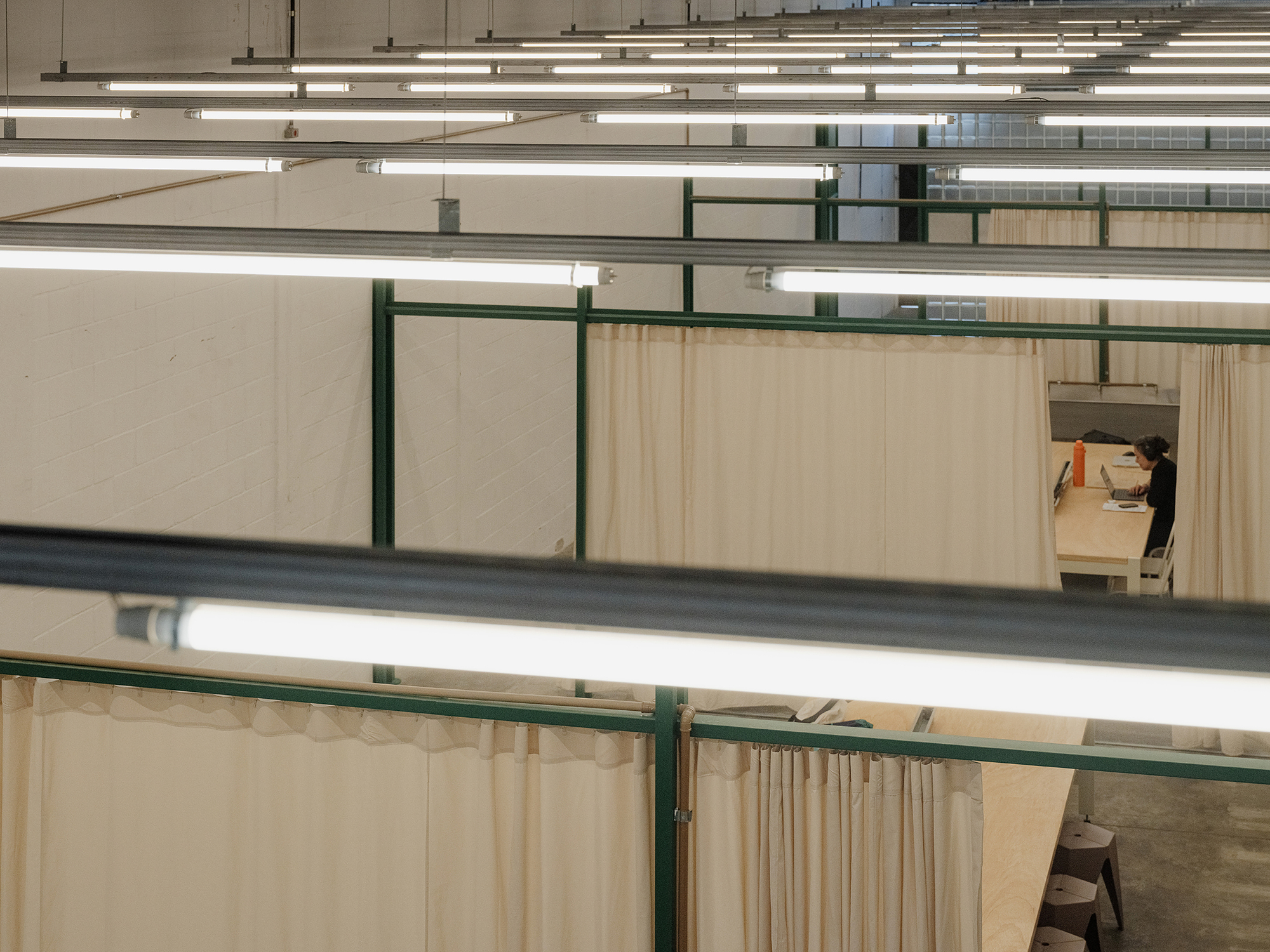 Elevated view across multiple fabric-partitioned workspaces with green steel frames and fluorescent lighting