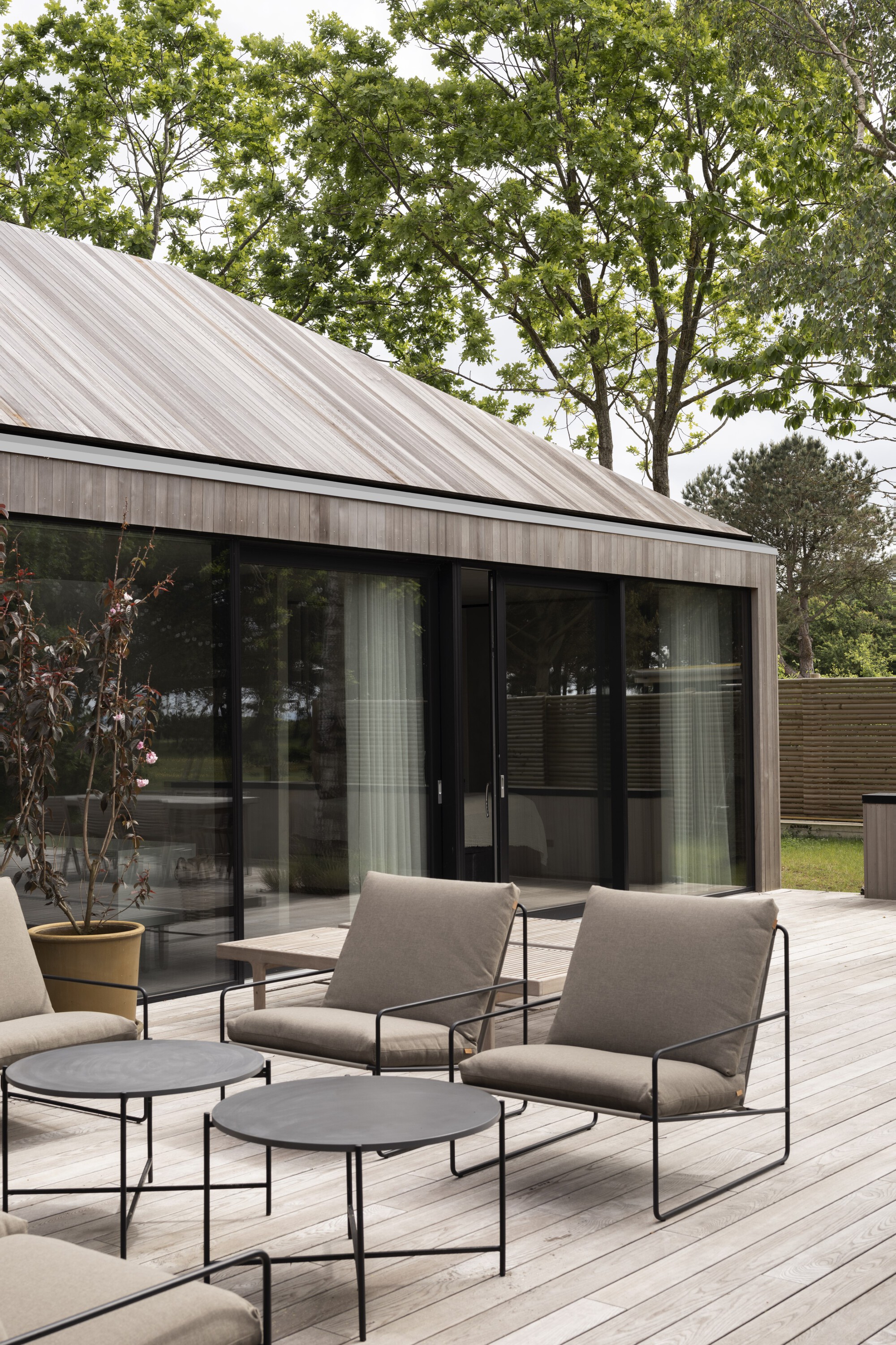 Outdoor seating area on pale wood decking with glass doors reflecting the surrounding green landscape