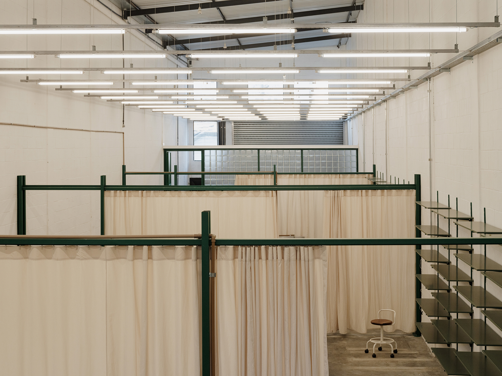 View through layered fabric partitions toward glazed mezzanine under grid of linear fluorescent fixtures