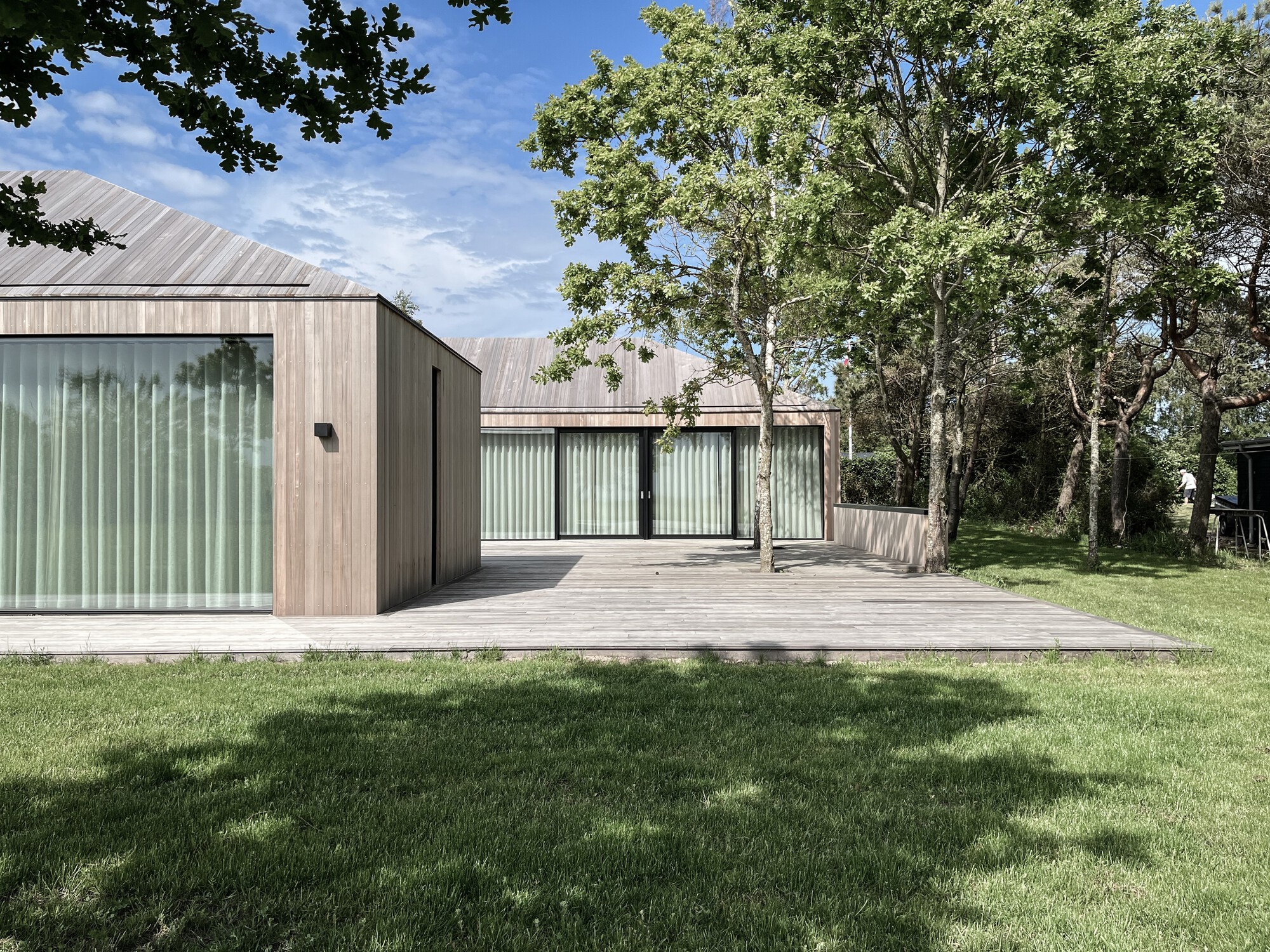 Gabled volume clad in vertical timber and corrugated metal viewed across mown lawn on a sunny day