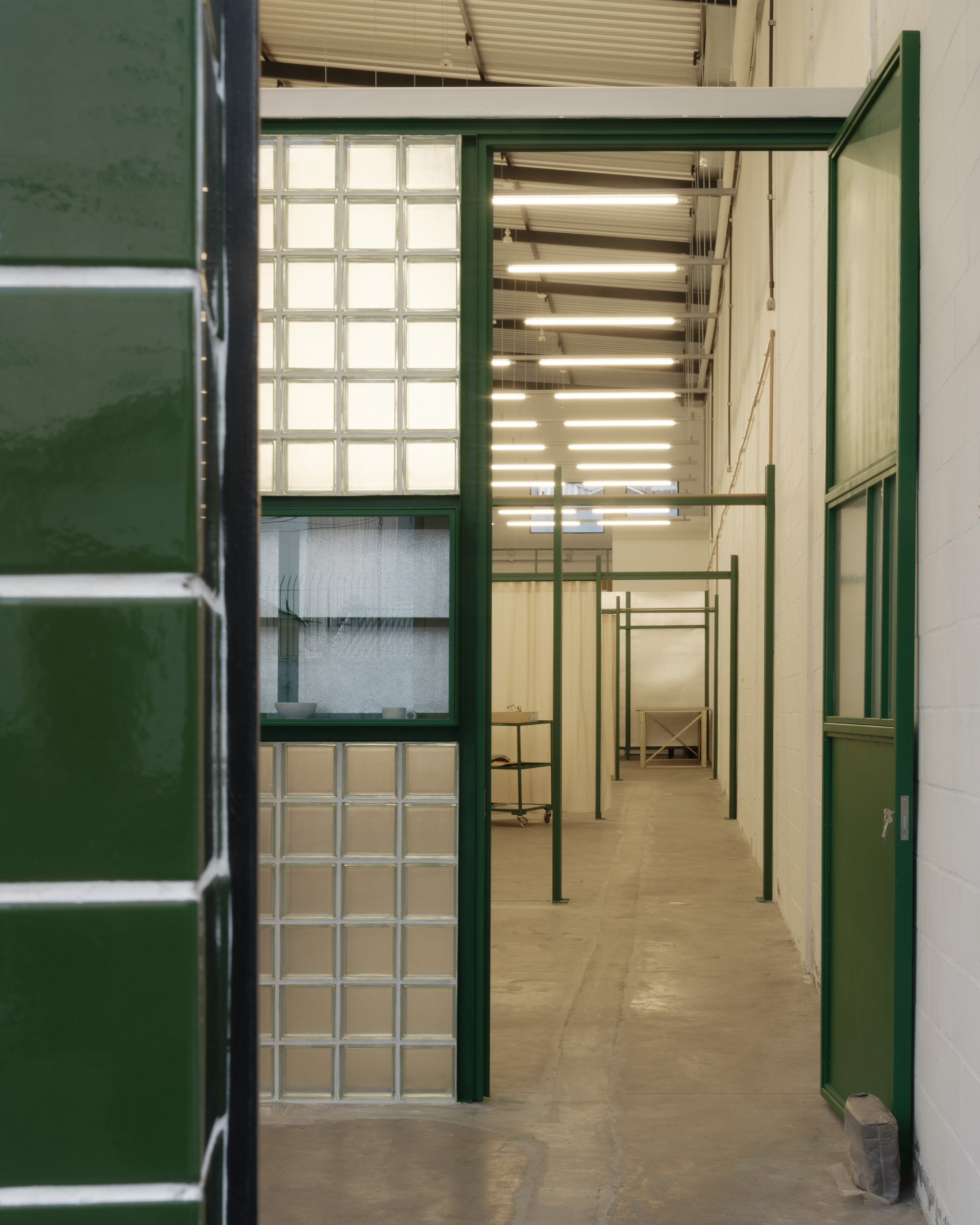 View through green steel framed doorway showing glass block wall and exposed linear ceiling lights above corridor