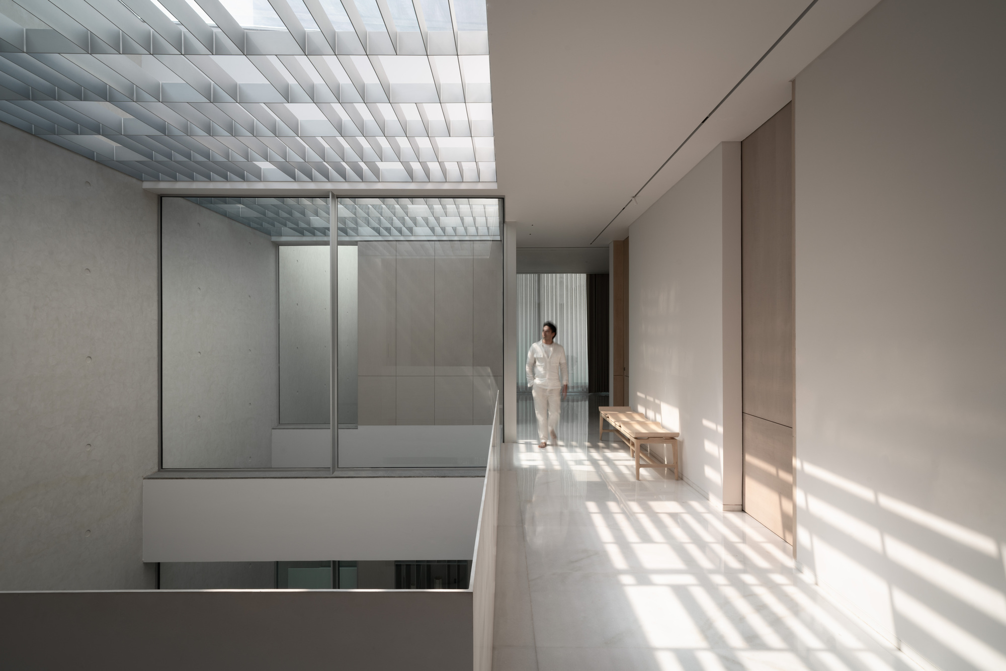 Upper corridor with baffled skylight casting striped shadows on white terrazzo flooring