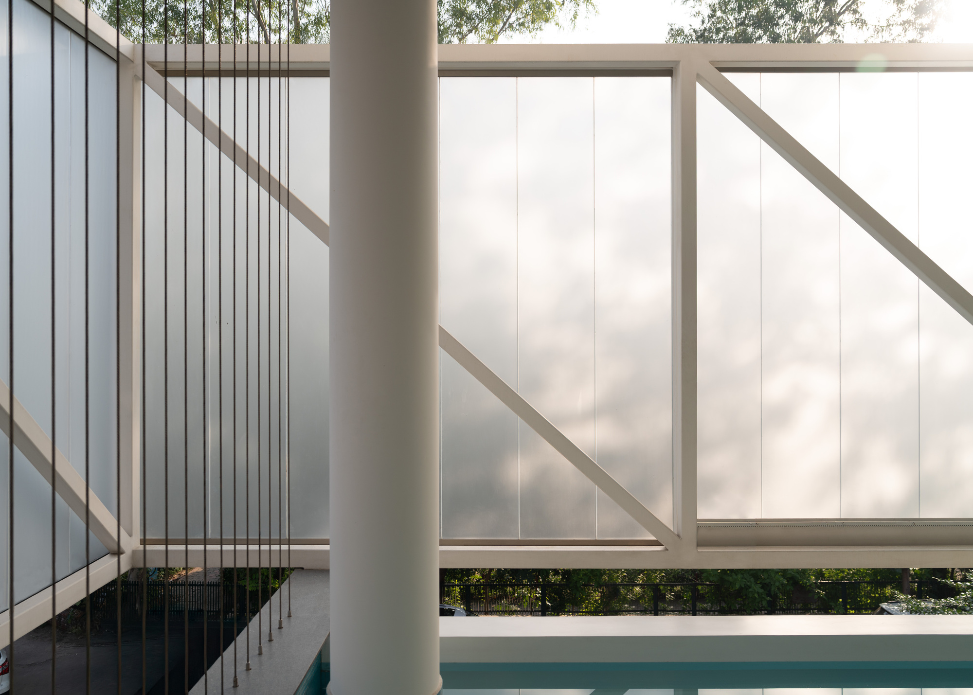 Swimming pool edge with white metal guardrails and suspended wire rods beneath a translucent screen
