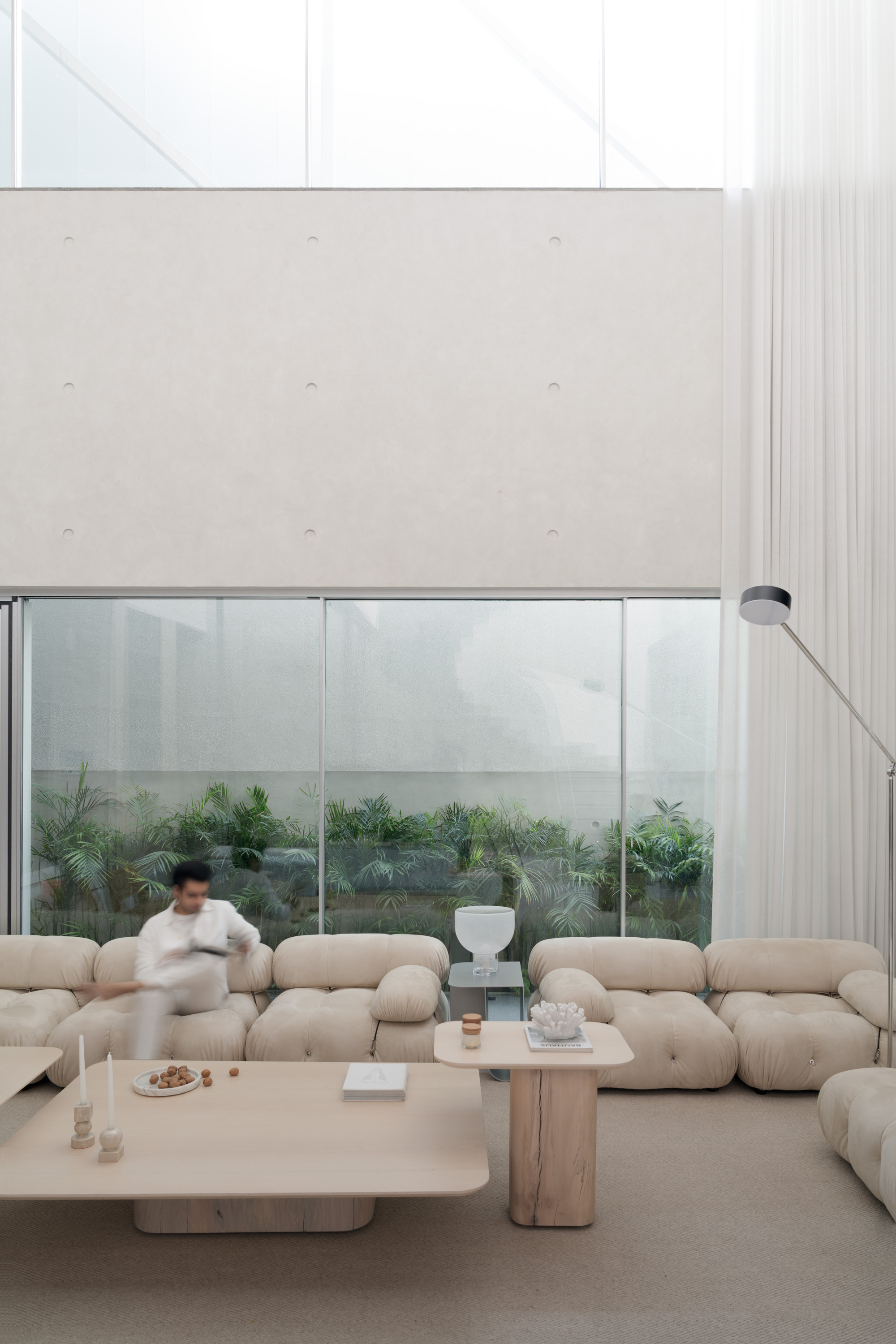 Double-height living room with curved modular sofa and translucent glass wall overlooking planted terrace