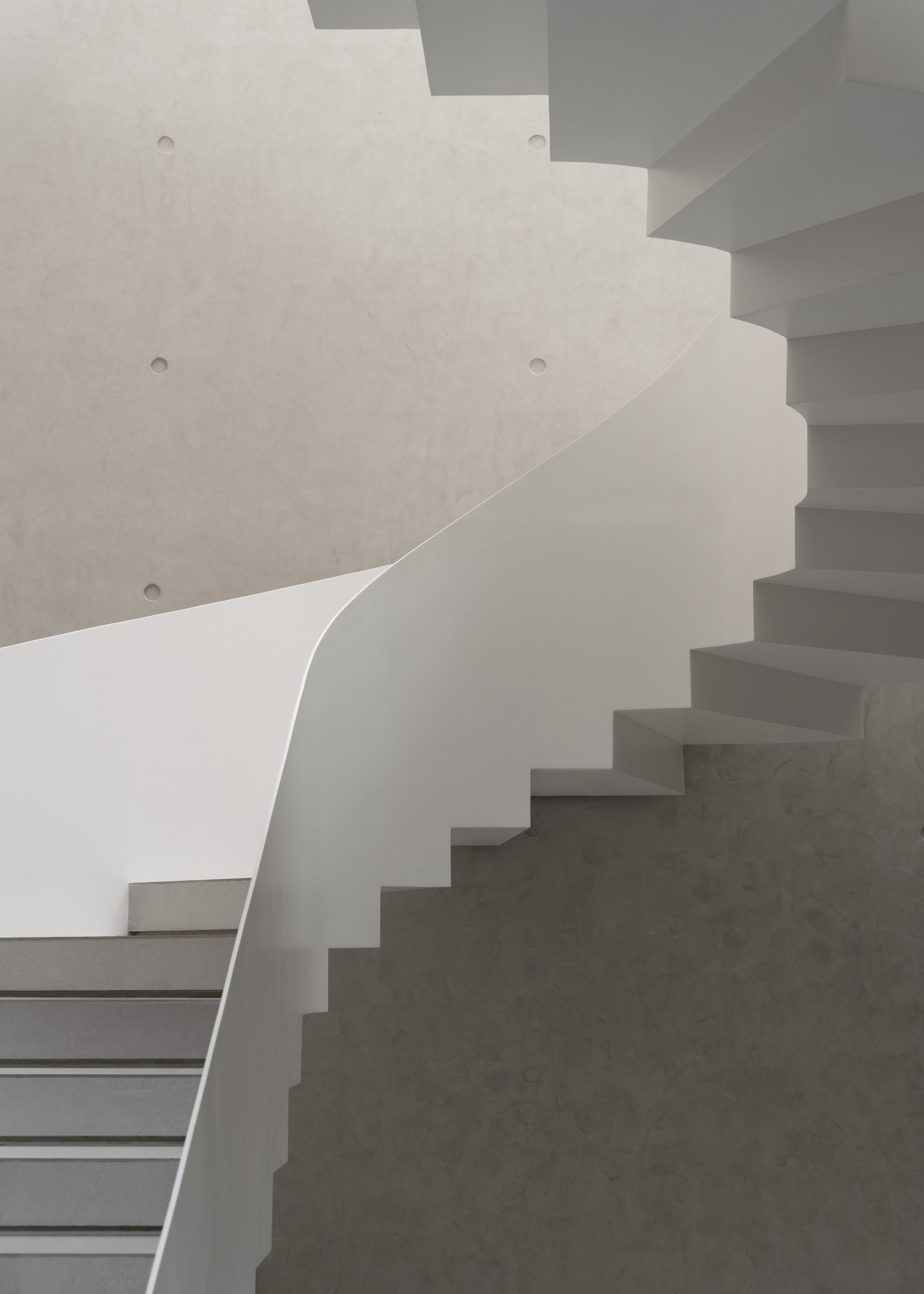 Overlapping concrete staircases with curved wall and recessed fasteners in soft daylight