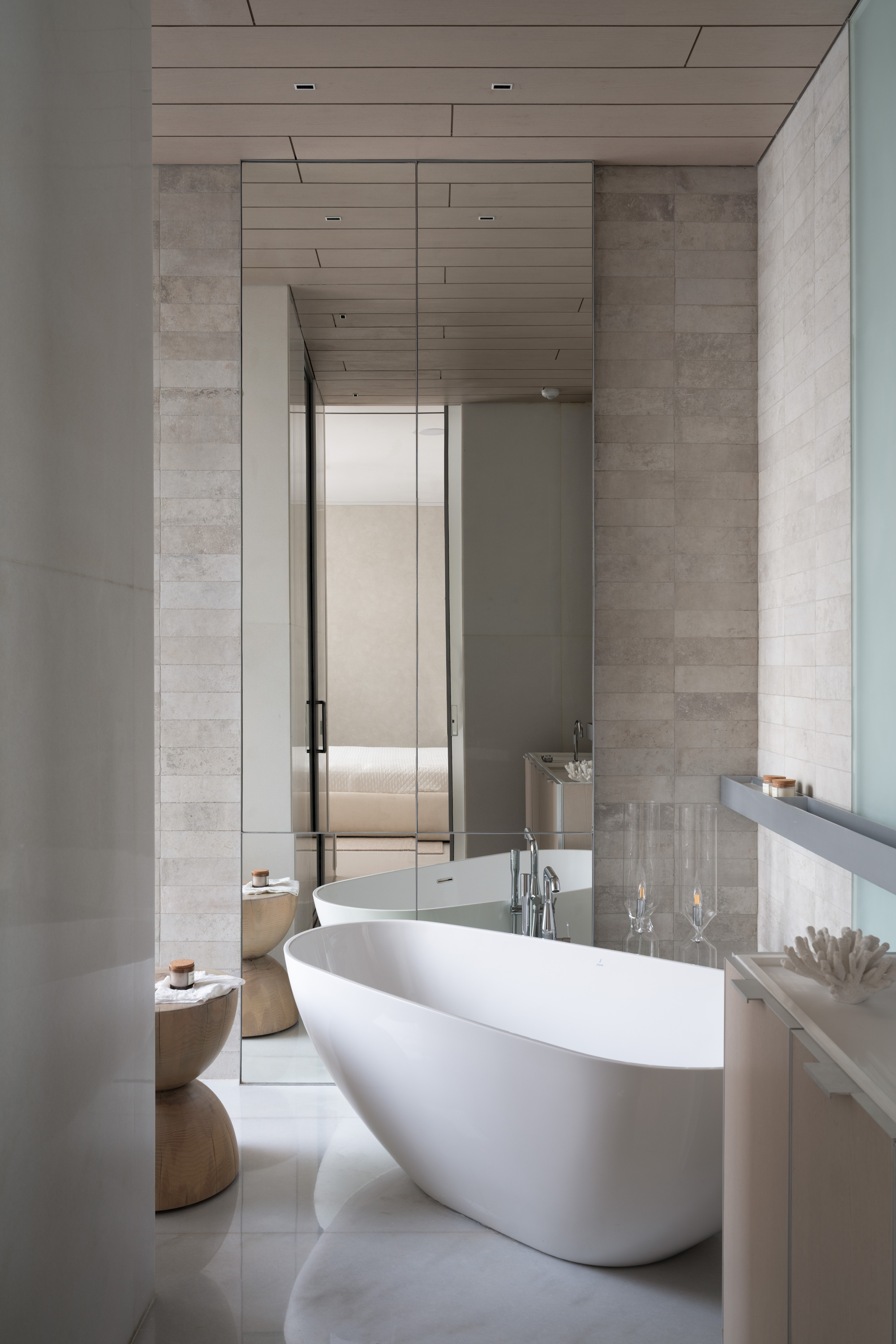 Bathroom with freestanding white tub flanked by horizontal stone tile and slatted timber ceiling