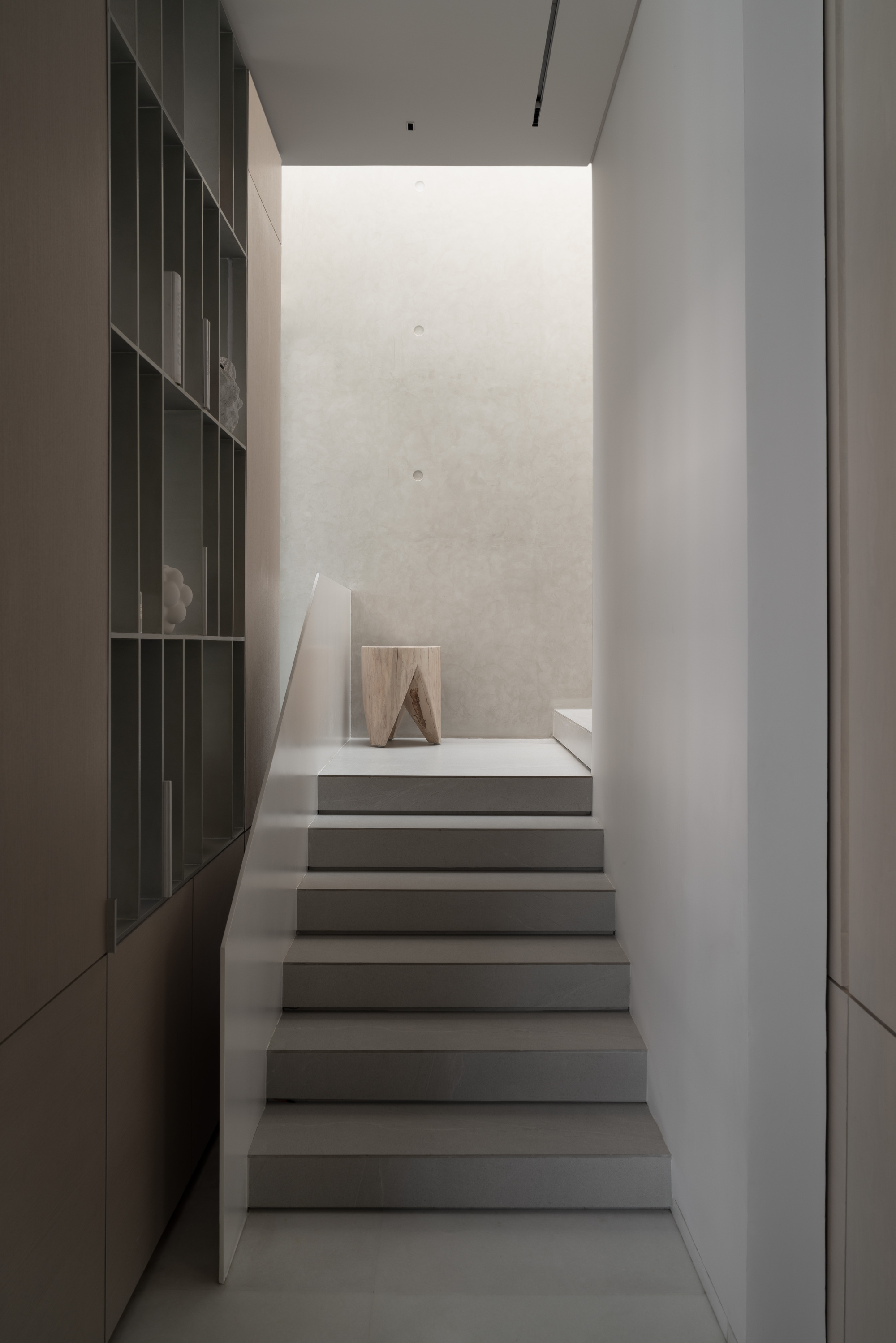 Staircase framed by dark shelving wall leading up to a landing with soft natural light