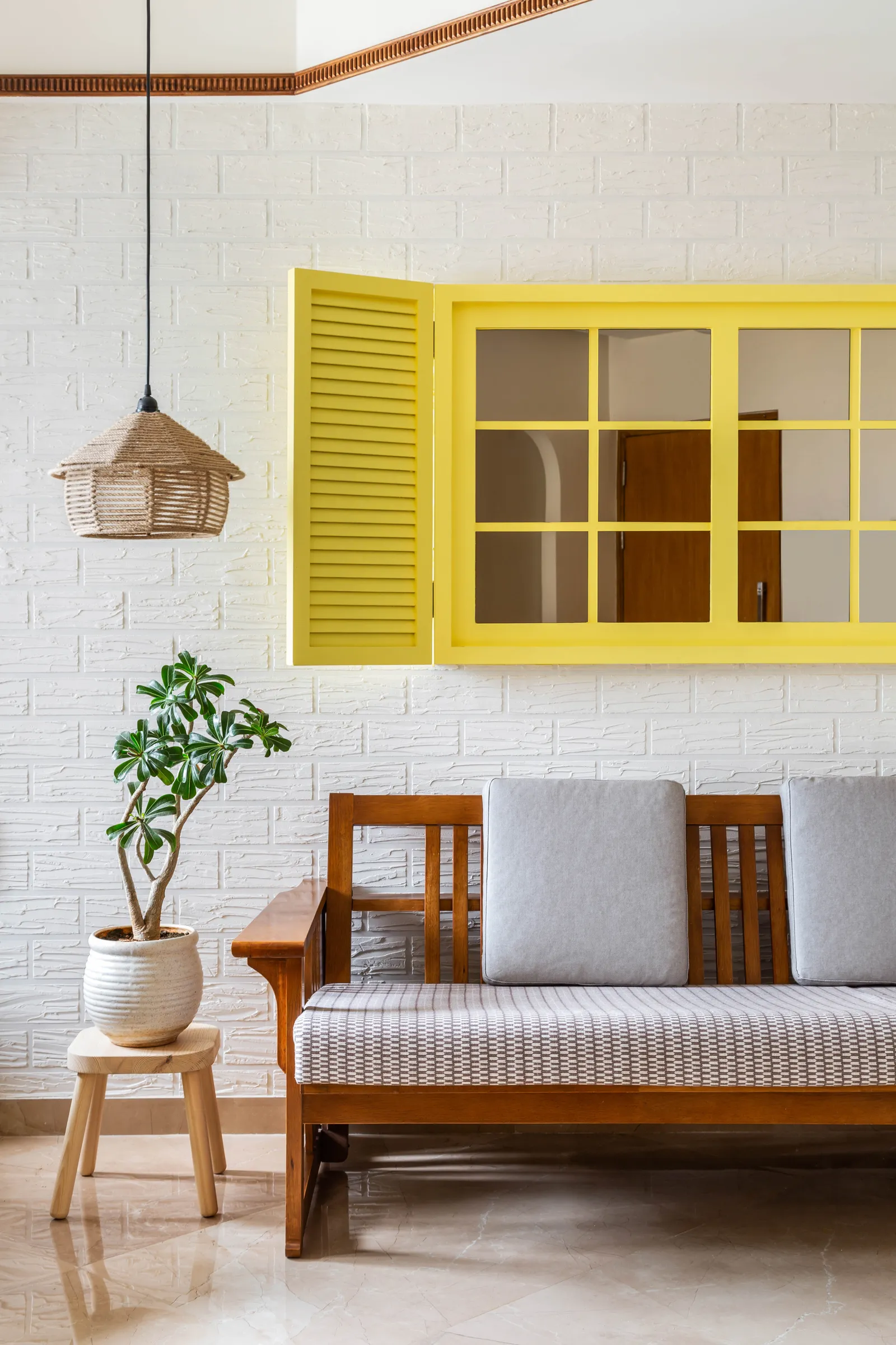 The warm colour scheme complements the accents of wood distributed through the design. The wall behind the sofa flaunts a bright yellow window with mirrors on a white brick wall. Anuja Kambli