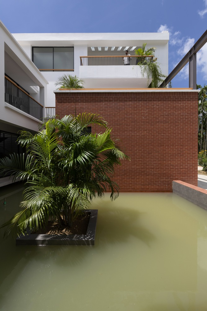 Courtyard water feature with red brick wall and planted palms beneath white residential volumes